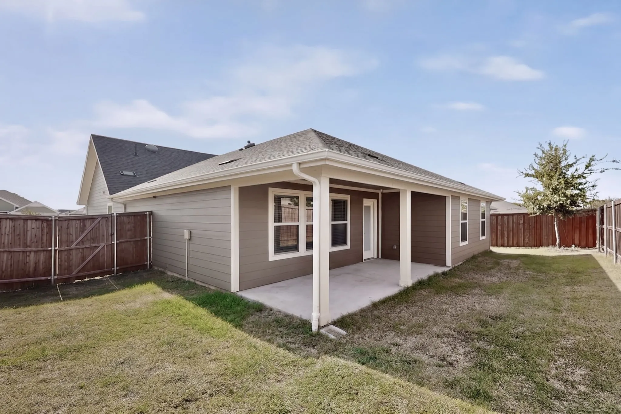 Covered patio with concrete flooring, framed by a wood fence, and a grass lawn