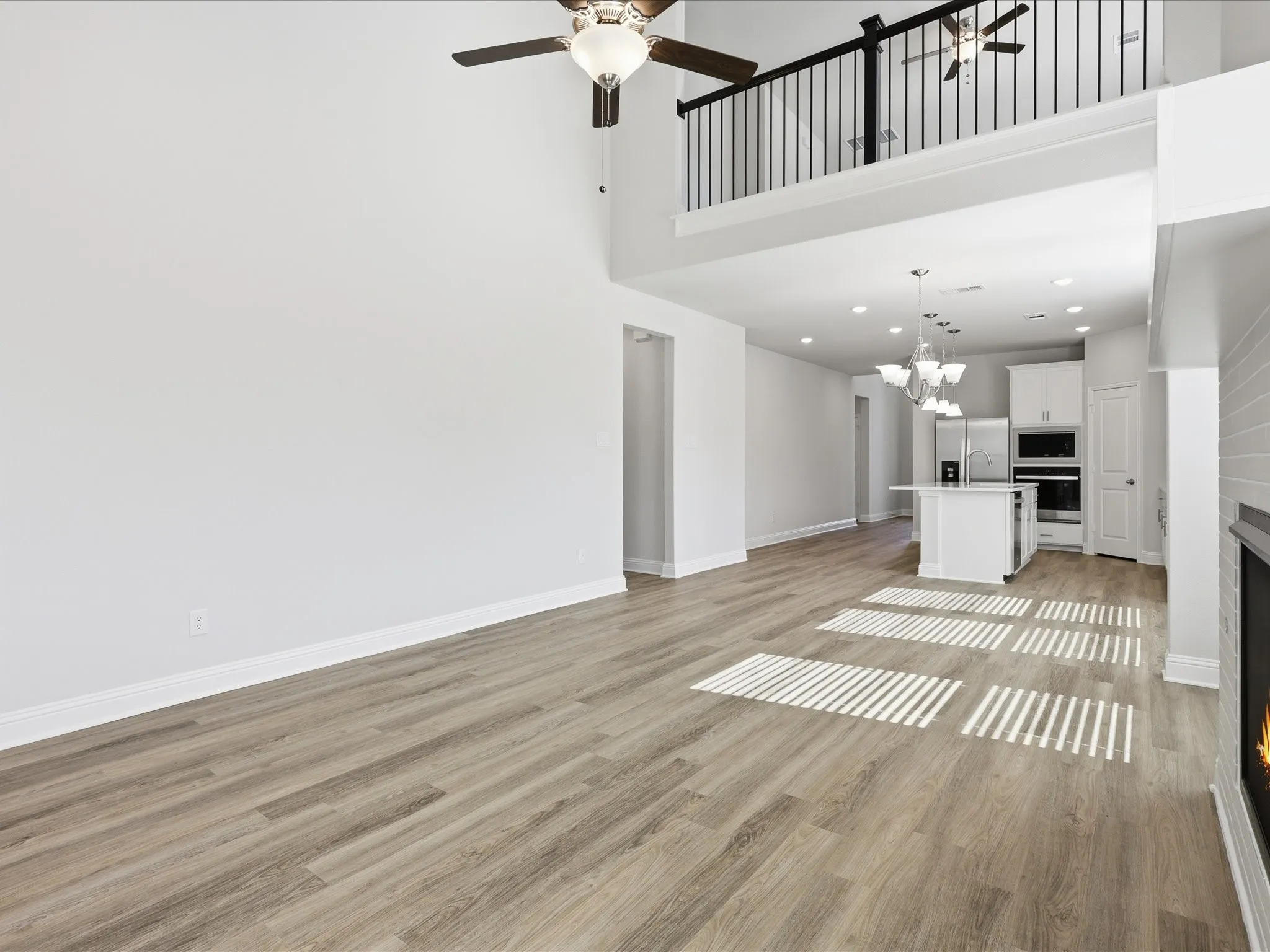 Unfurnished living room with a lit fireplace, light wood-type flooring, a ceiling fan, a towering ceiling, and a chandelier