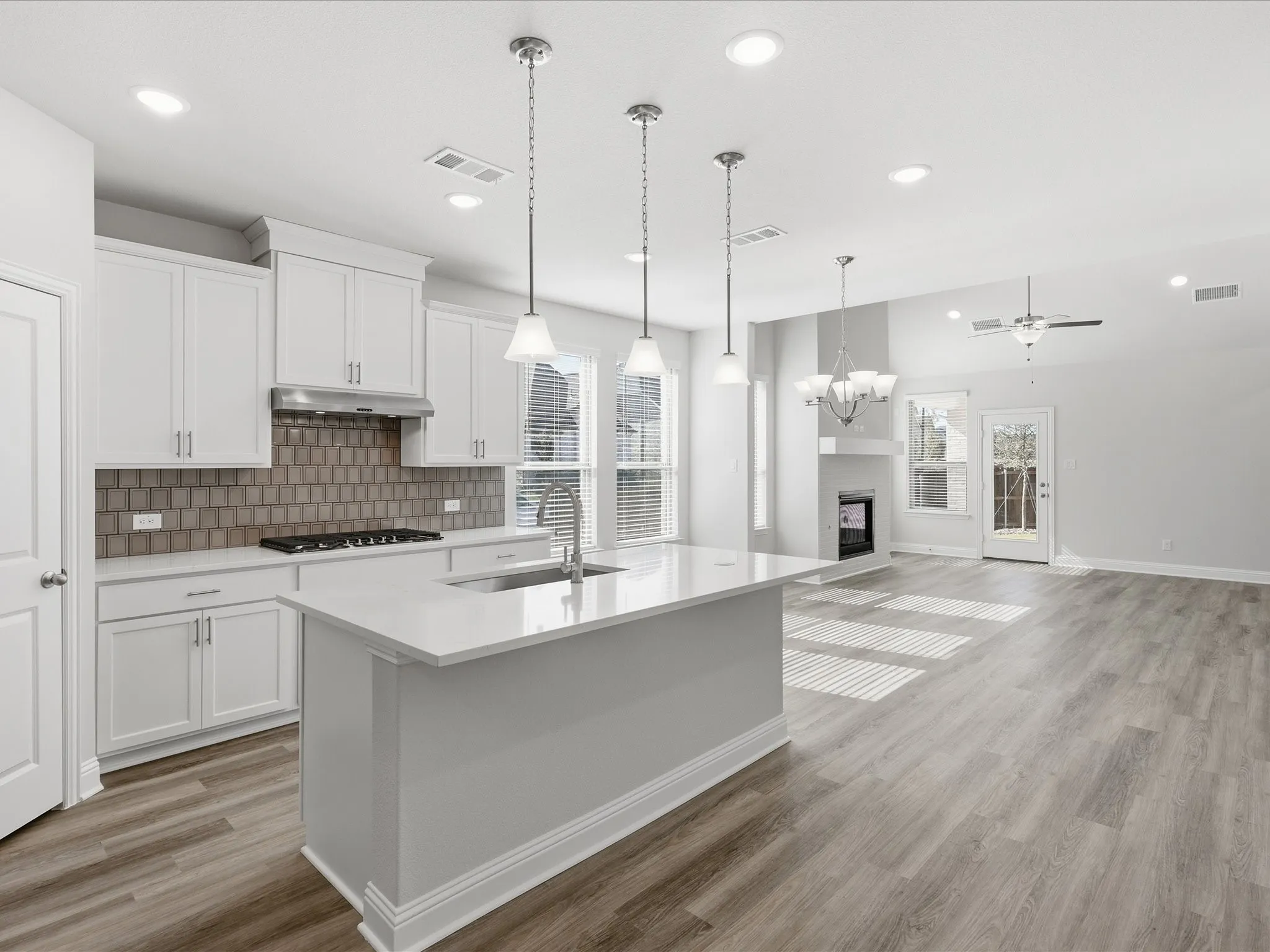 Kitchen featuring white cabinetry, tasteful backsplash, decorative light fixtures, a center island with sink, and open floor plan