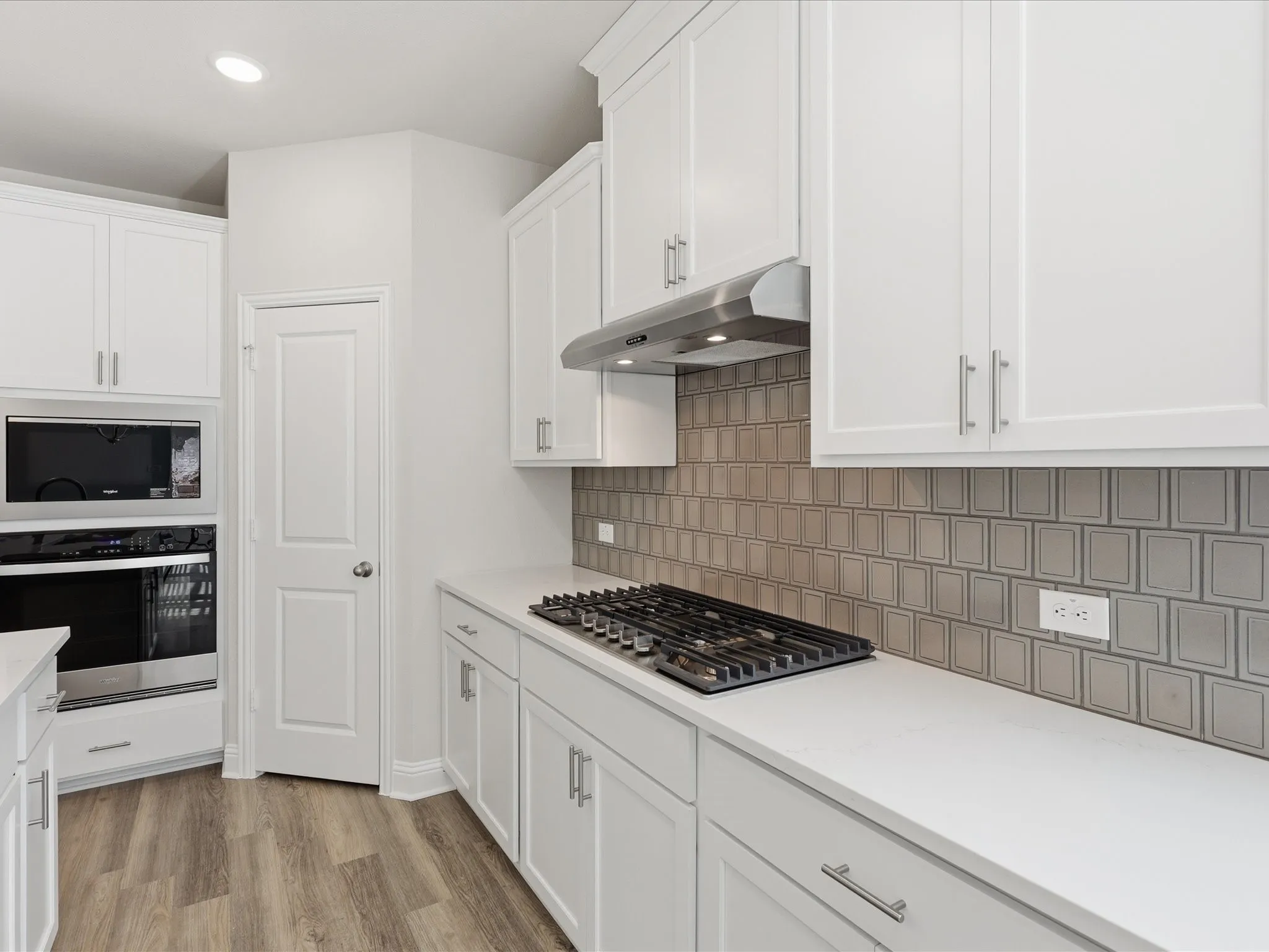 Kitchen with white cabinetry, stainless steel appliances, light wood-style flooring, backsplash, and under cabinet range hood