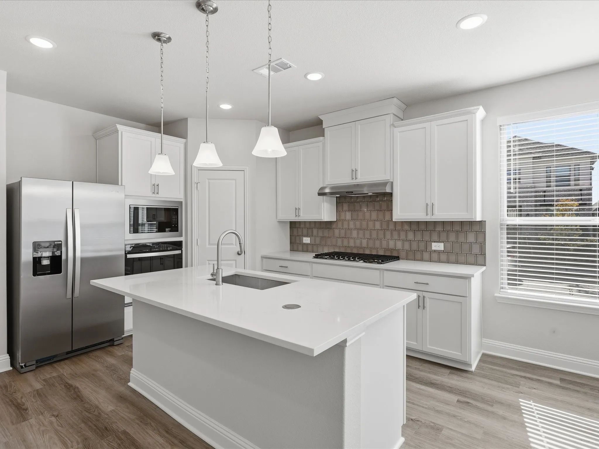 Kitchen featuring appliances with stainless steel finishes, decorative backsplash, an island with sink, pendant lighting, and white cabinets