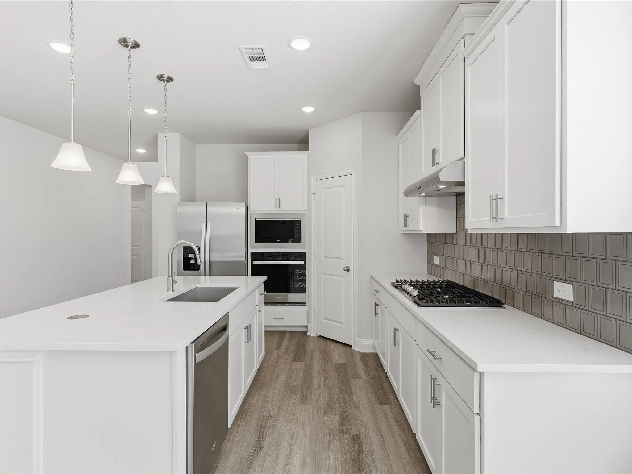 Kitchen featuring decorative light fixtures, appliances with stainless steel finishes, light wood finished floors, white cabinets, and a kitchen island with sink
