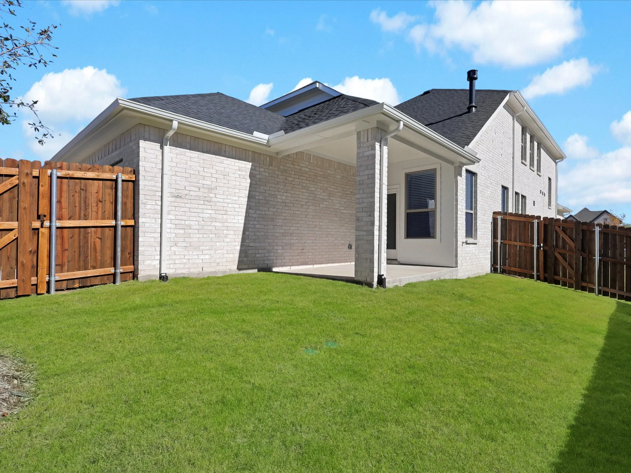 Back of property featuring a gate, a patio area, and brick siding