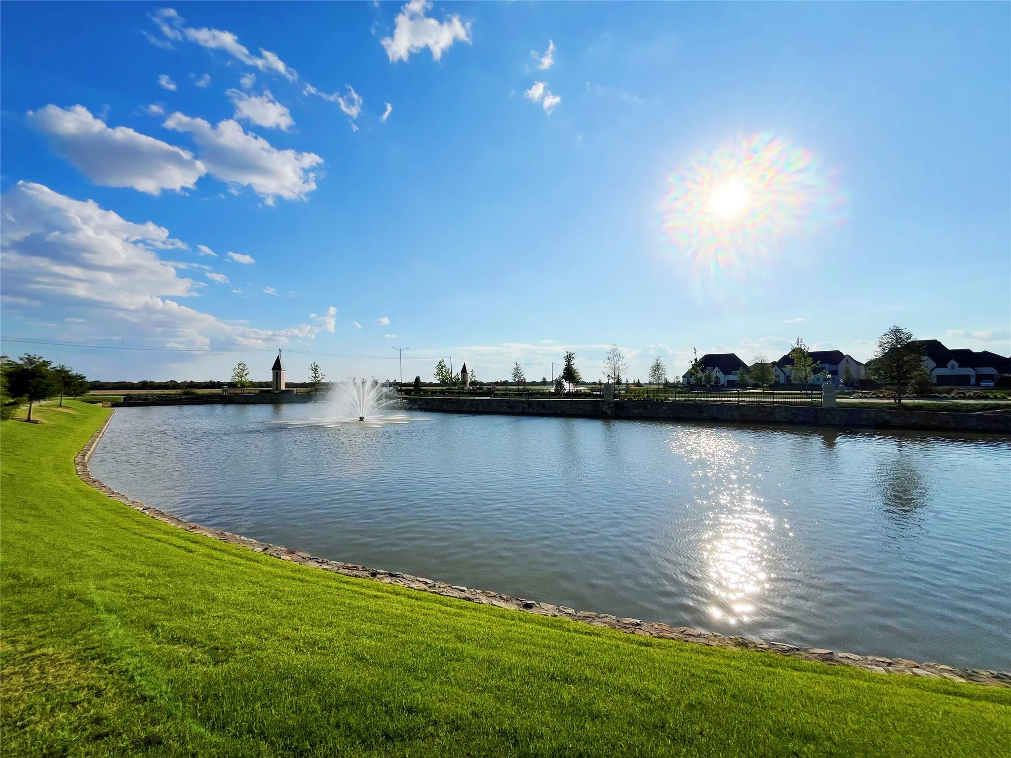 Expansive water feature with a central fountain, bordered by a manicured grassy bank and a stone-edged perimeter