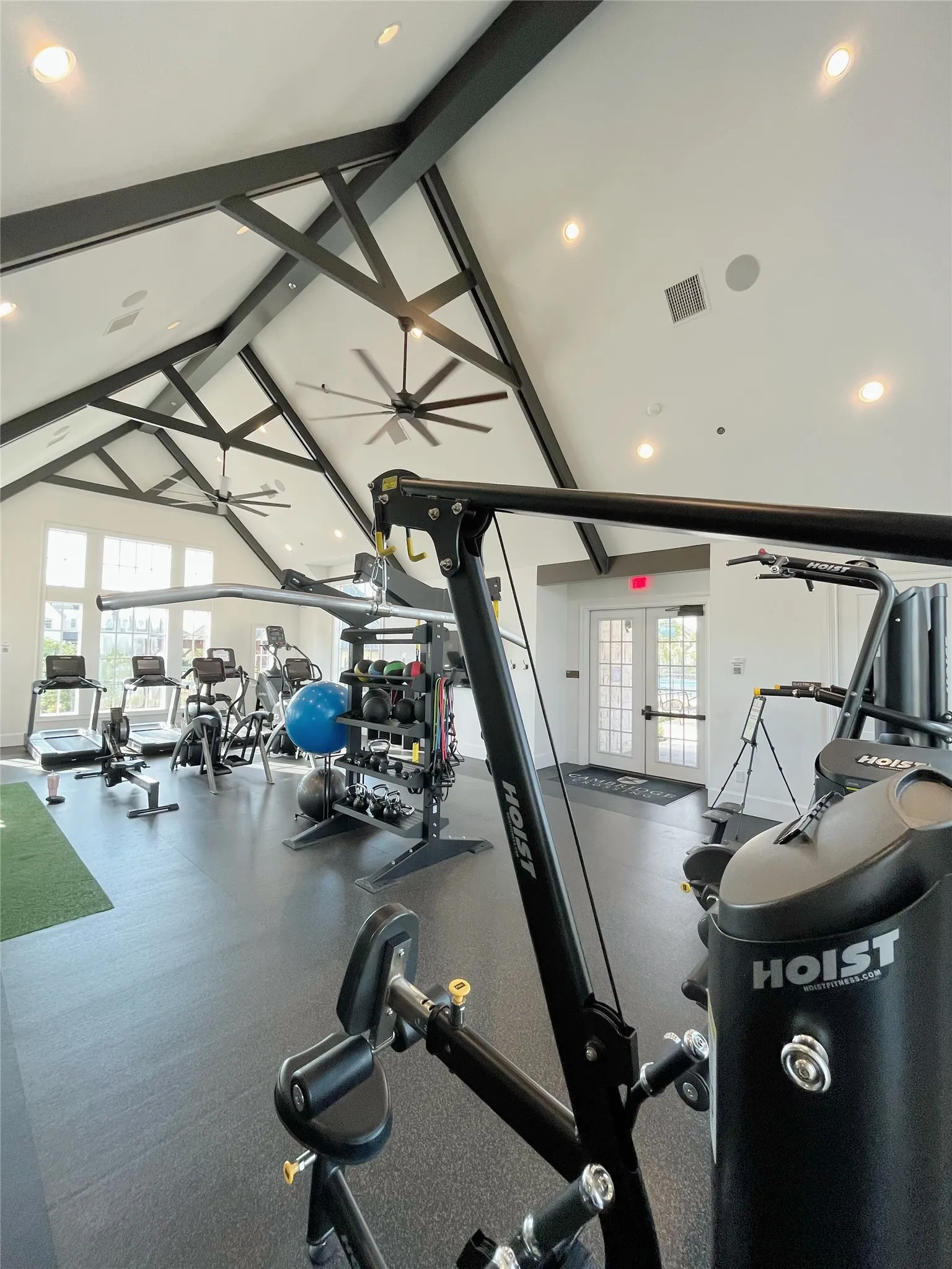 Vaulted ceiling with exposed beams, recessed lighting, industrial ceiling fans, rubber flooring, and French doors