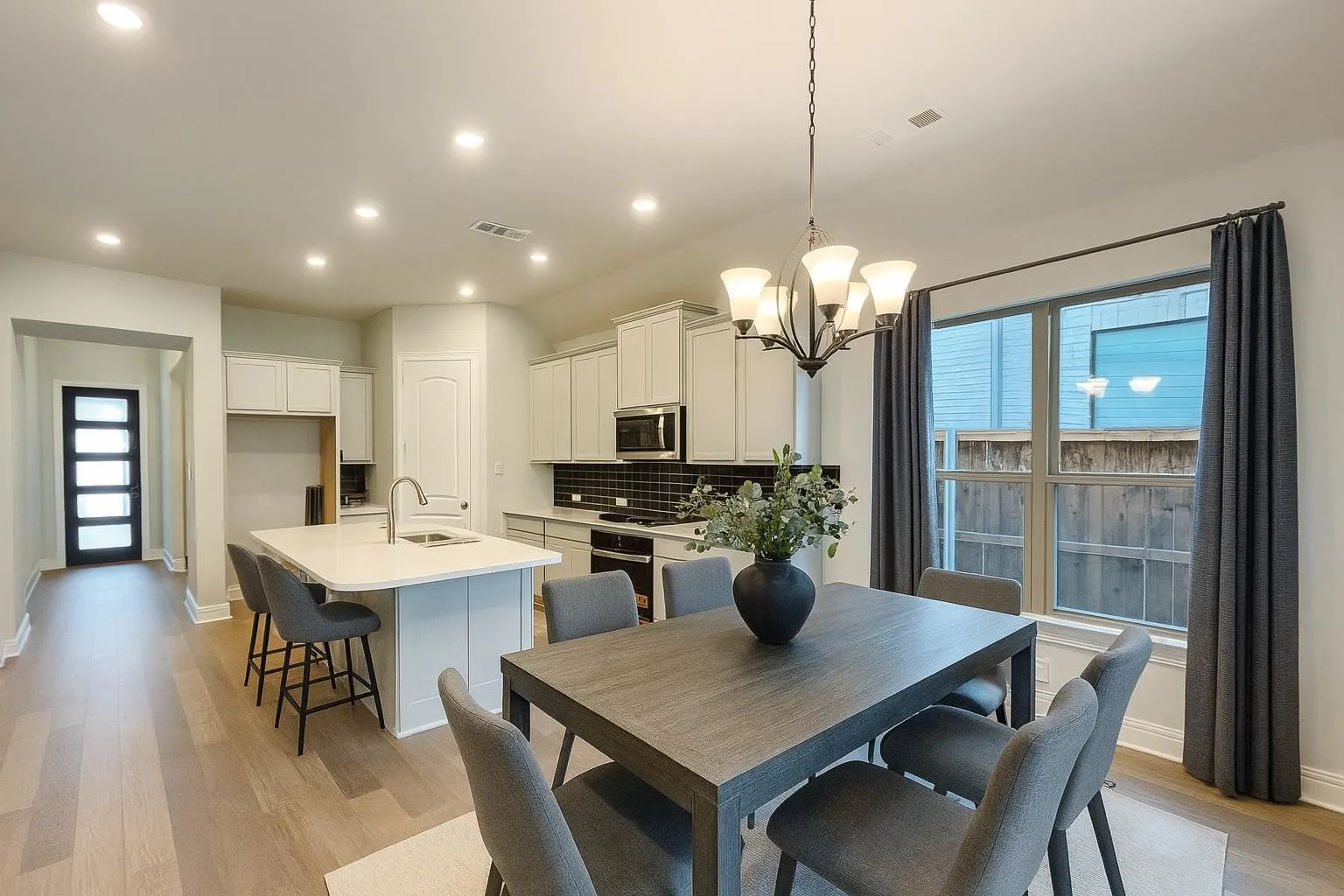 Open-concept living area featuring wood-finish flooring, recessed lighting, a kitchen island with seating, white cabinetry, and a black subway tile backsplash