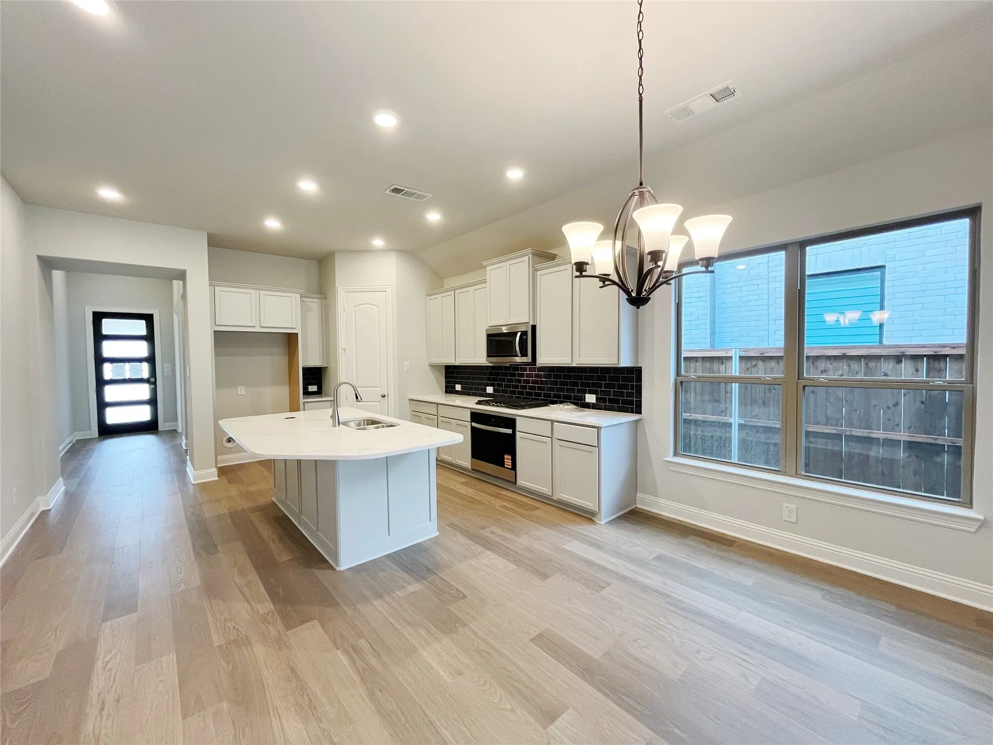Contemporary kitchen featuring an island with an integrated sink, white cabinetry, black subway tile backsplash, and stainless steel appliances