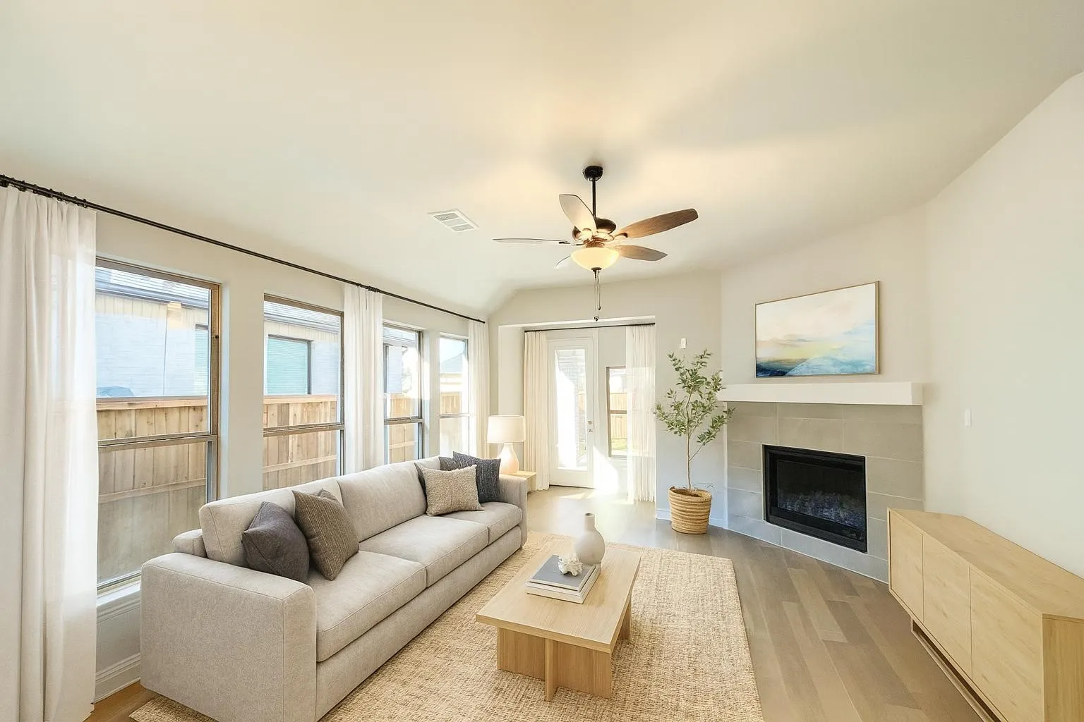 Vaulted ceiling featuring a ceiling fan, fireplace with a mantle, multiple windows, and wood-finish flooring