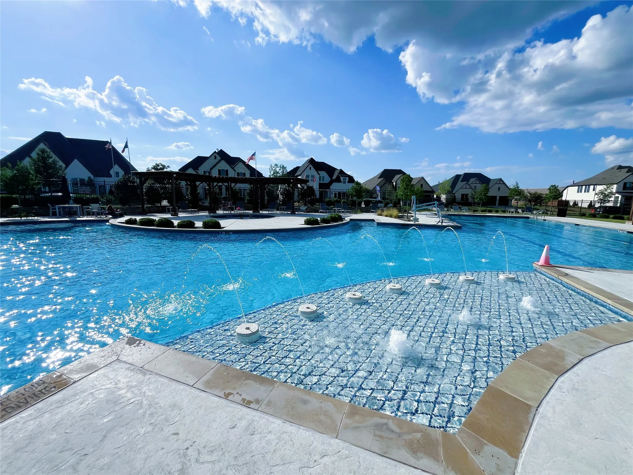 Expansive resort-style pool featuring multiple water features, a separate shallow water entry with spray jets, and surrounding concrete decking