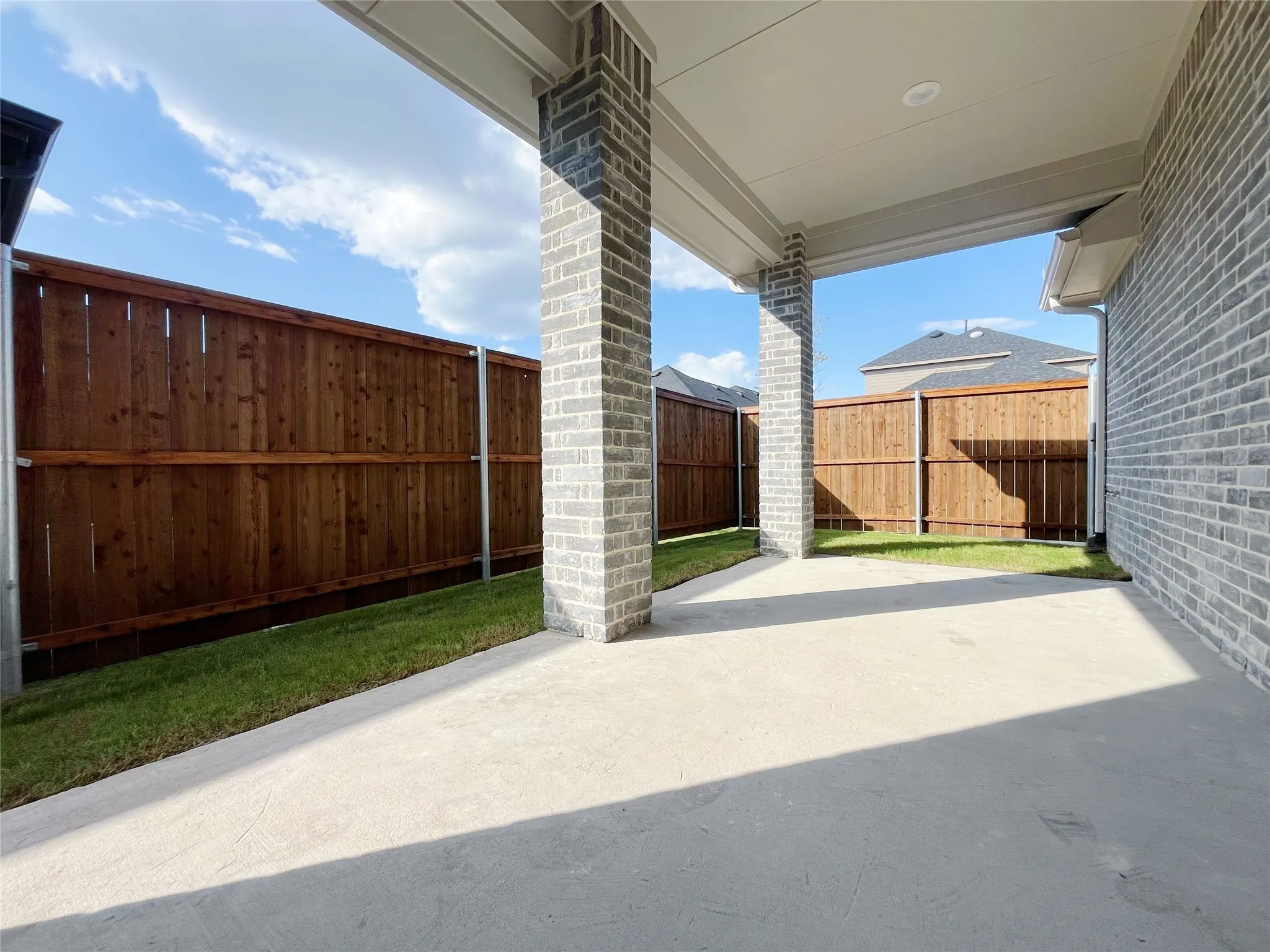Covered patio with recessed lighting, concrete flooring, brick columns, and a wood privacy fence