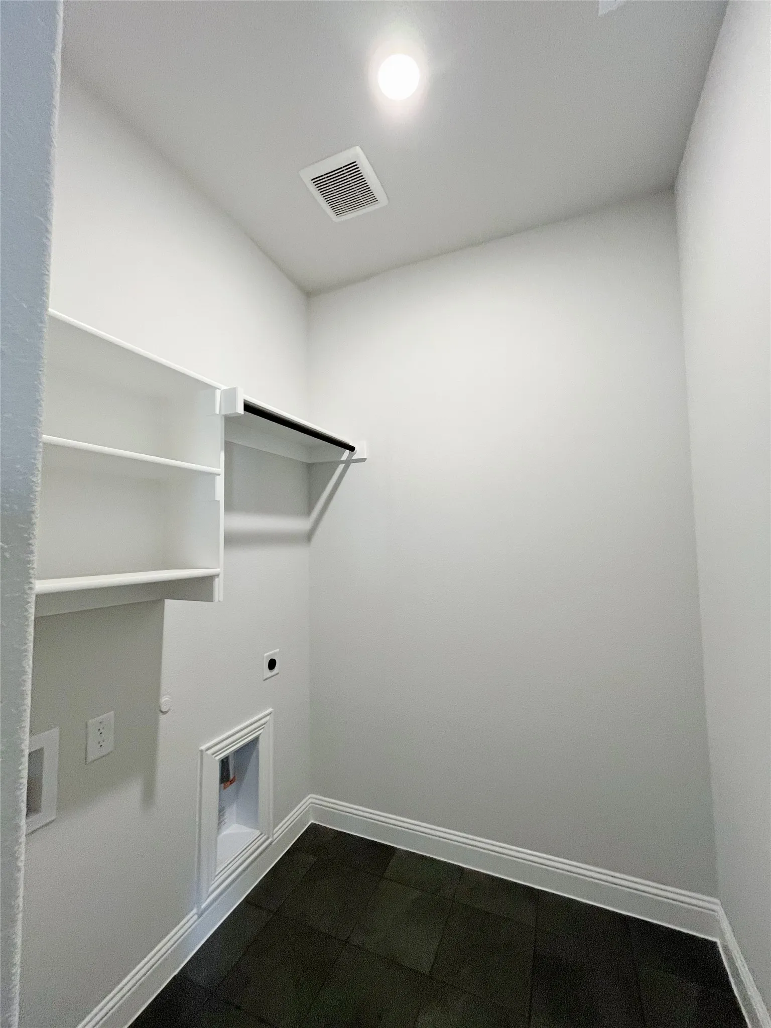Built-in shelving, hanging rod, and dark tile flooring