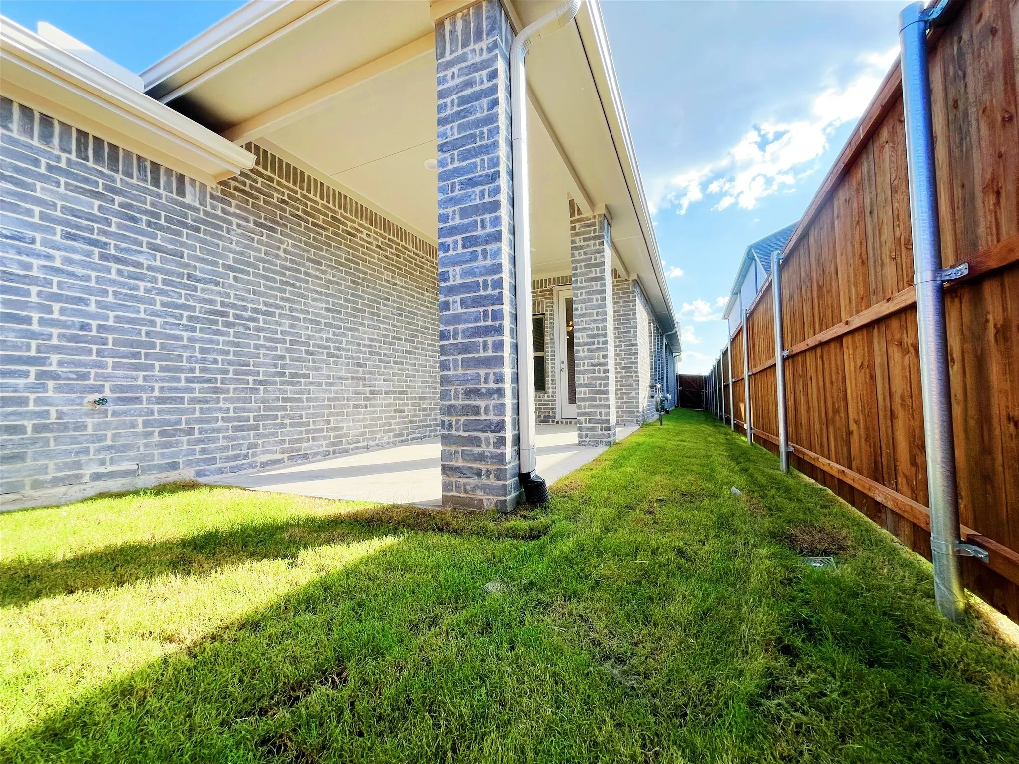 Covered patio with concrete flooring, supported by brick columns, featuring a full-height brick exterior