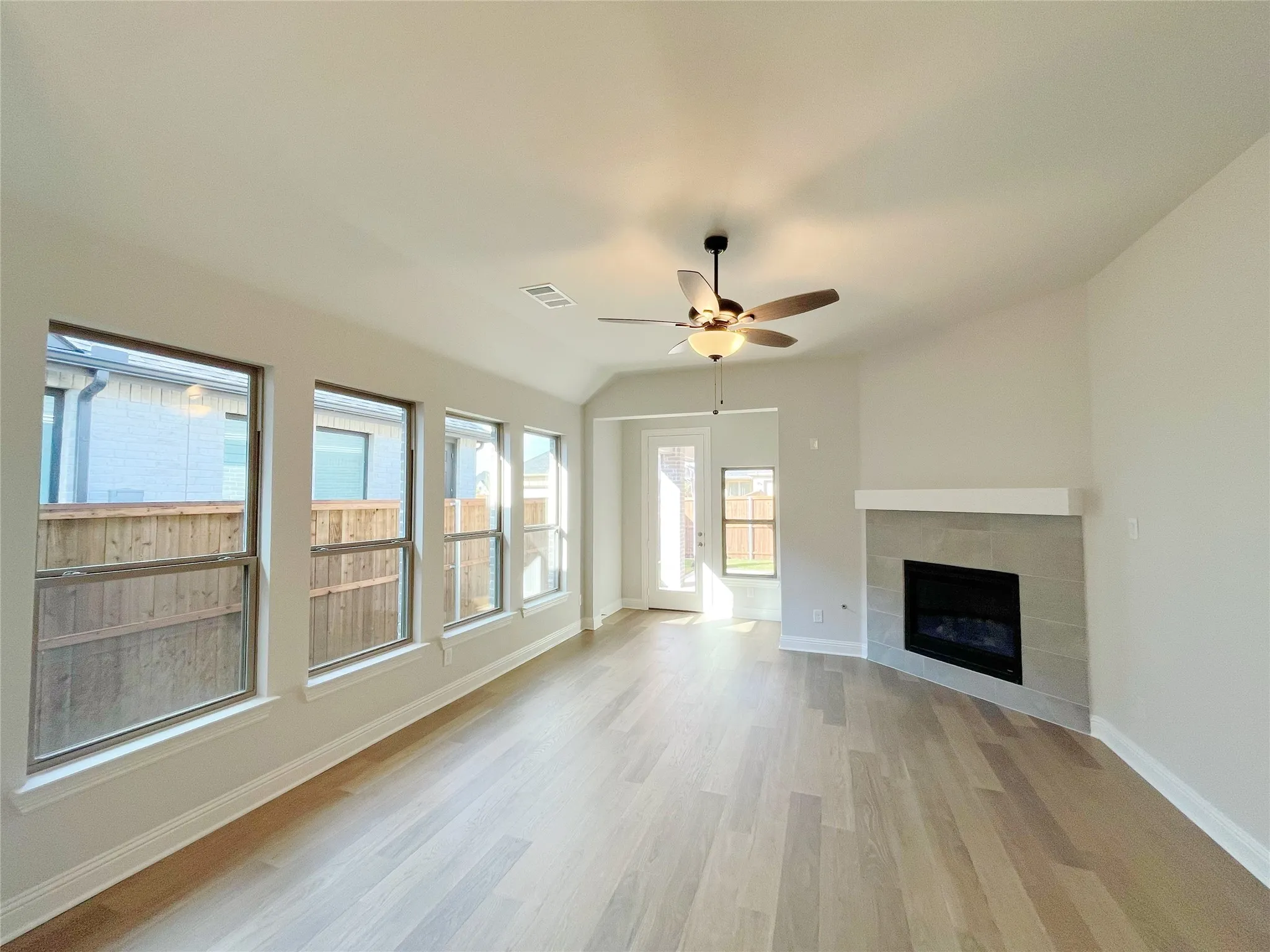 Vaulted ceiling with an attached ceiling fan, wood-finish flooring, a tiled fireplace with a mantel, and multiple windows