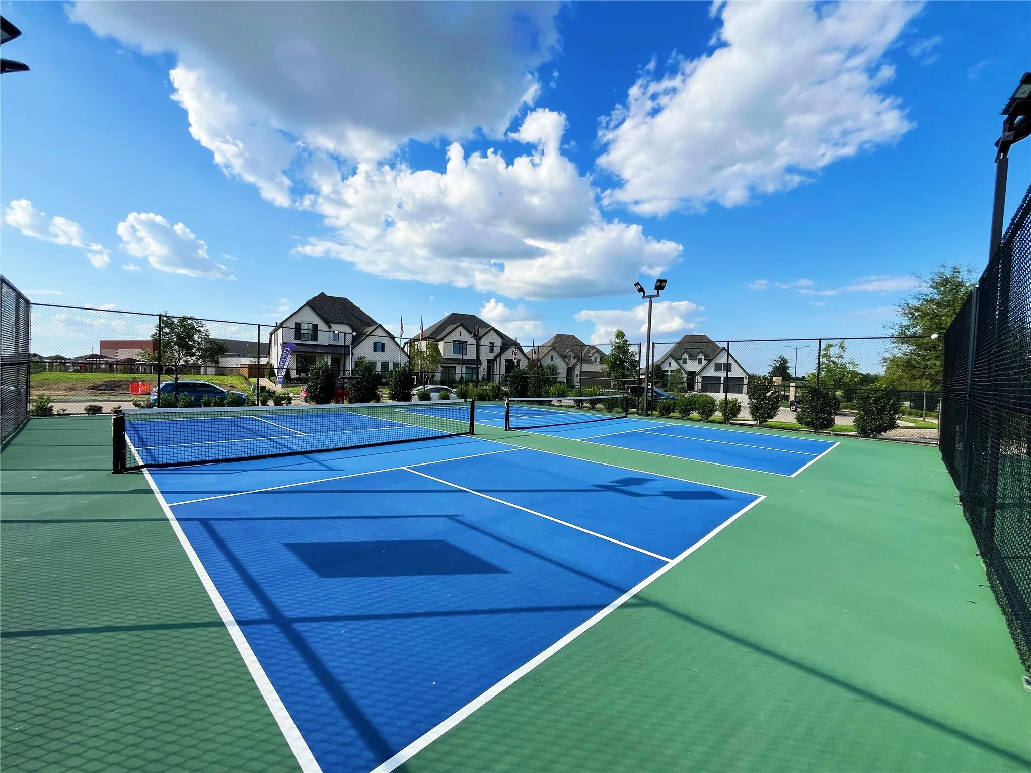 Recreational courts featuring a blue and green playing surface, white demarcation lines, and black netting