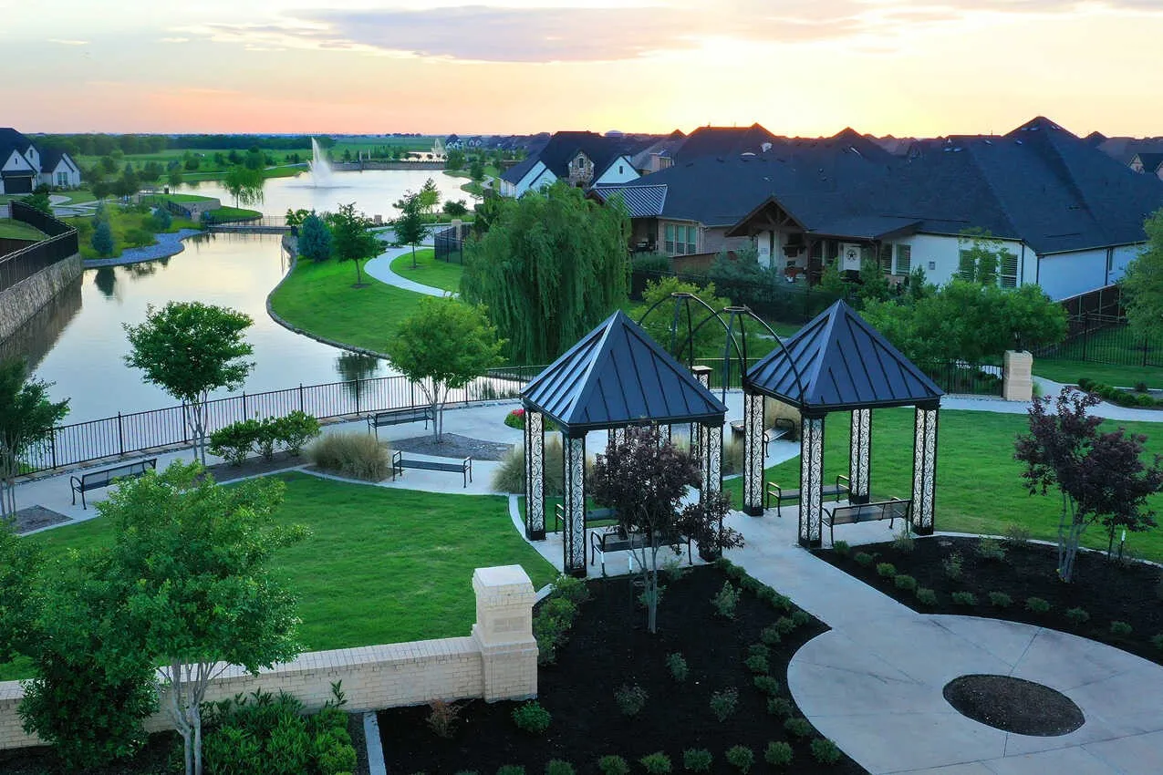Community green space featuring two covered pavilions, paved pathways, and a water feature with a fountain