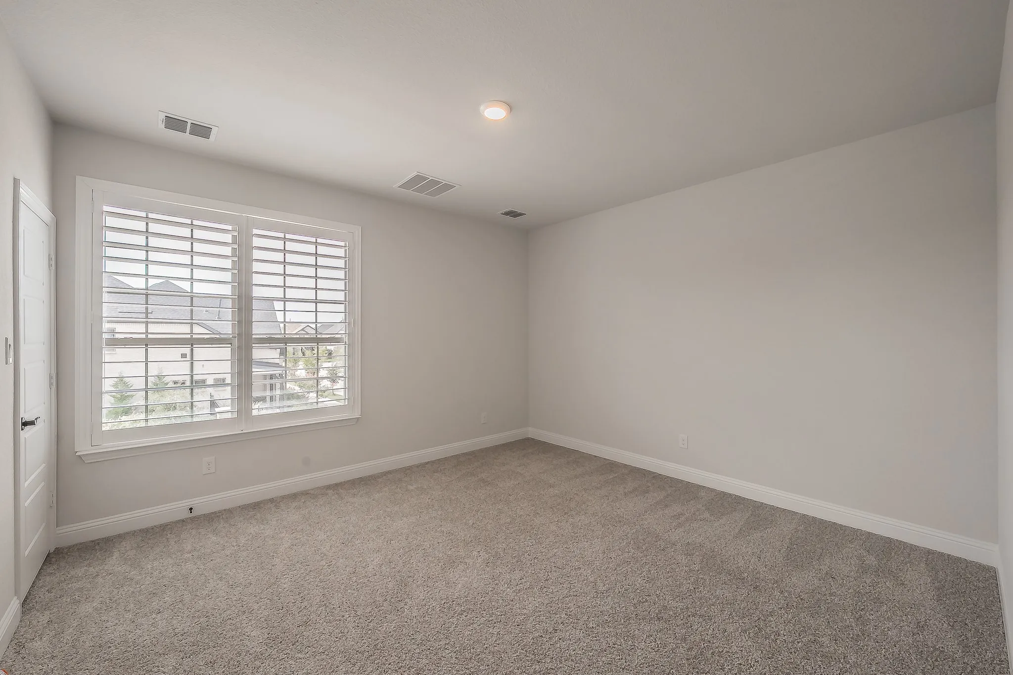 Neutral paint palette, plush carpet flooring, window with plantation shutters, recessed lighting, and a white interior door with dark hardware