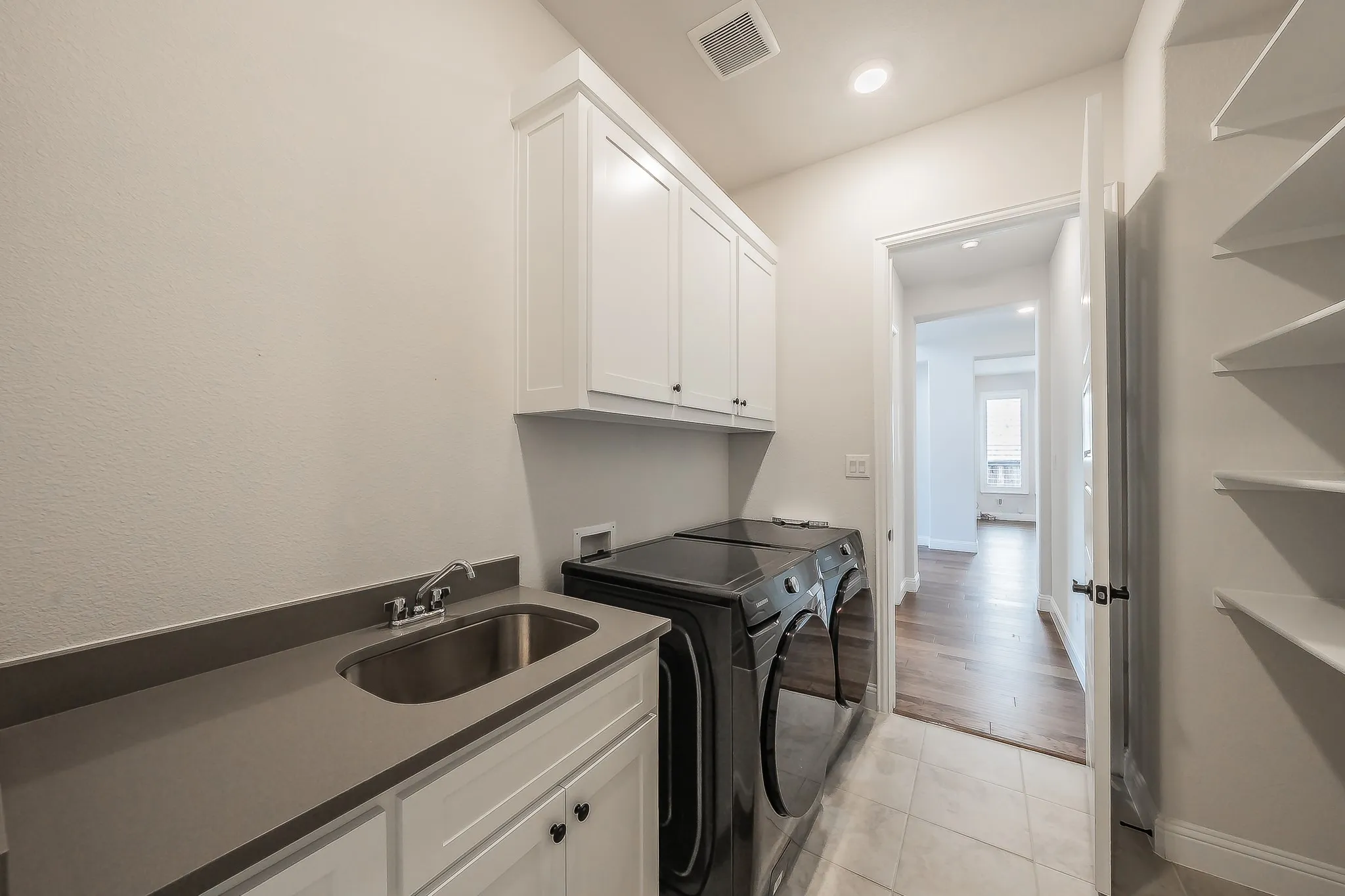 Utility room featuring white cabinetry, a built-in sink with a countertop, tiled flooring, and integrated shelving