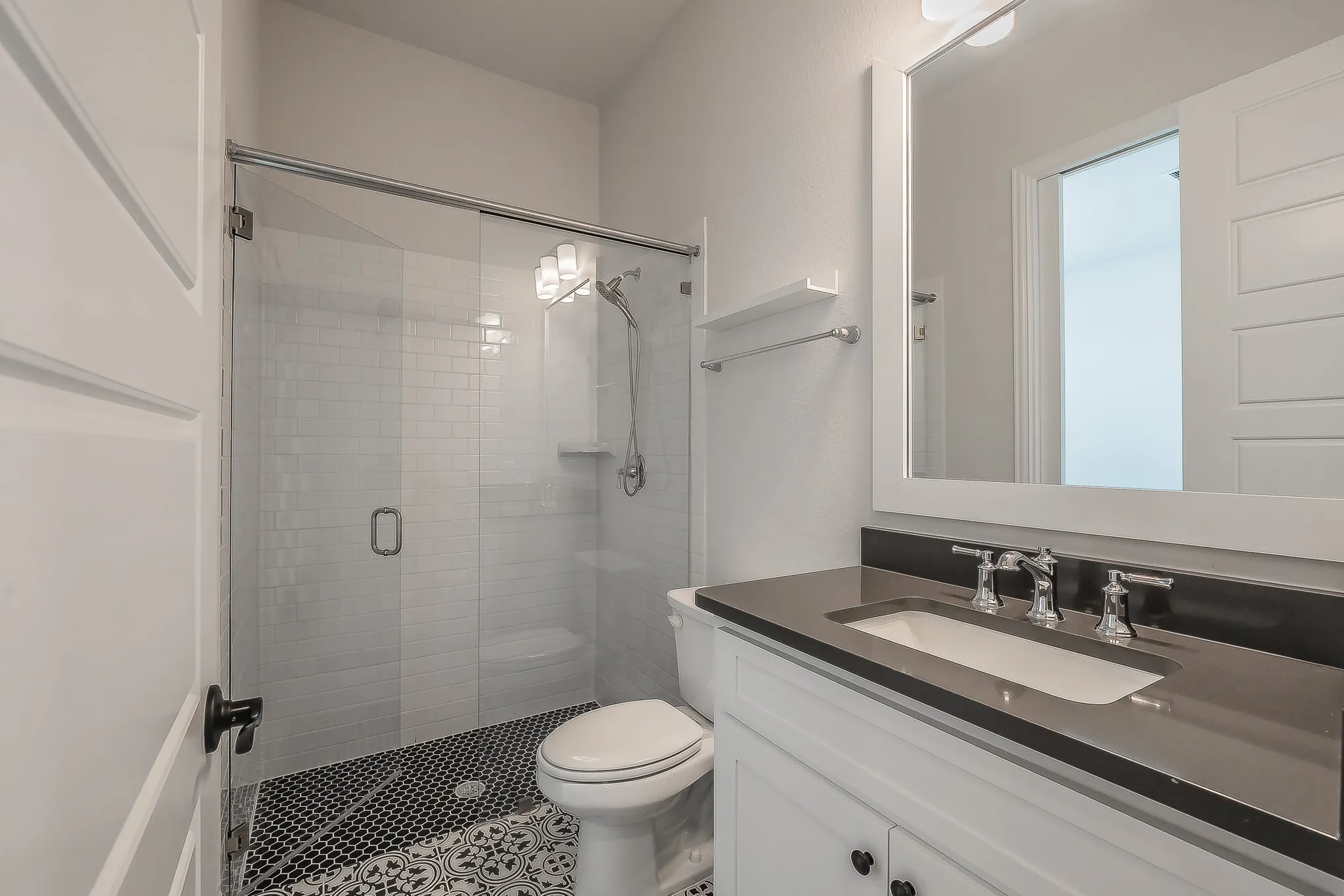 1st floor full bathroom.  Glass-enclosed shower with subway tile, mosaic tile flooring, single vanity with dark countertop, and framed mirror