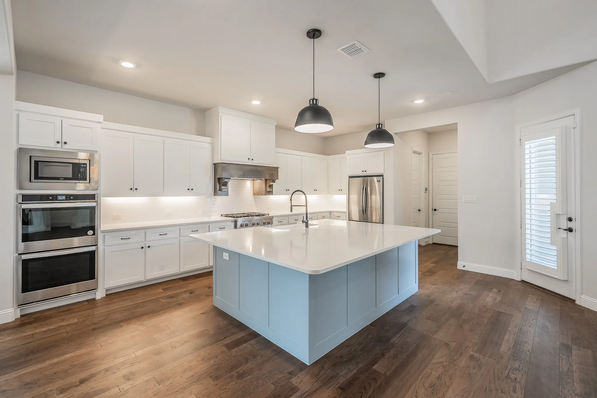 Kitchen featuring a light blue island, white cabinetry, integrated stainless steel appliances, wood-finish flooring, and pendant lighting
