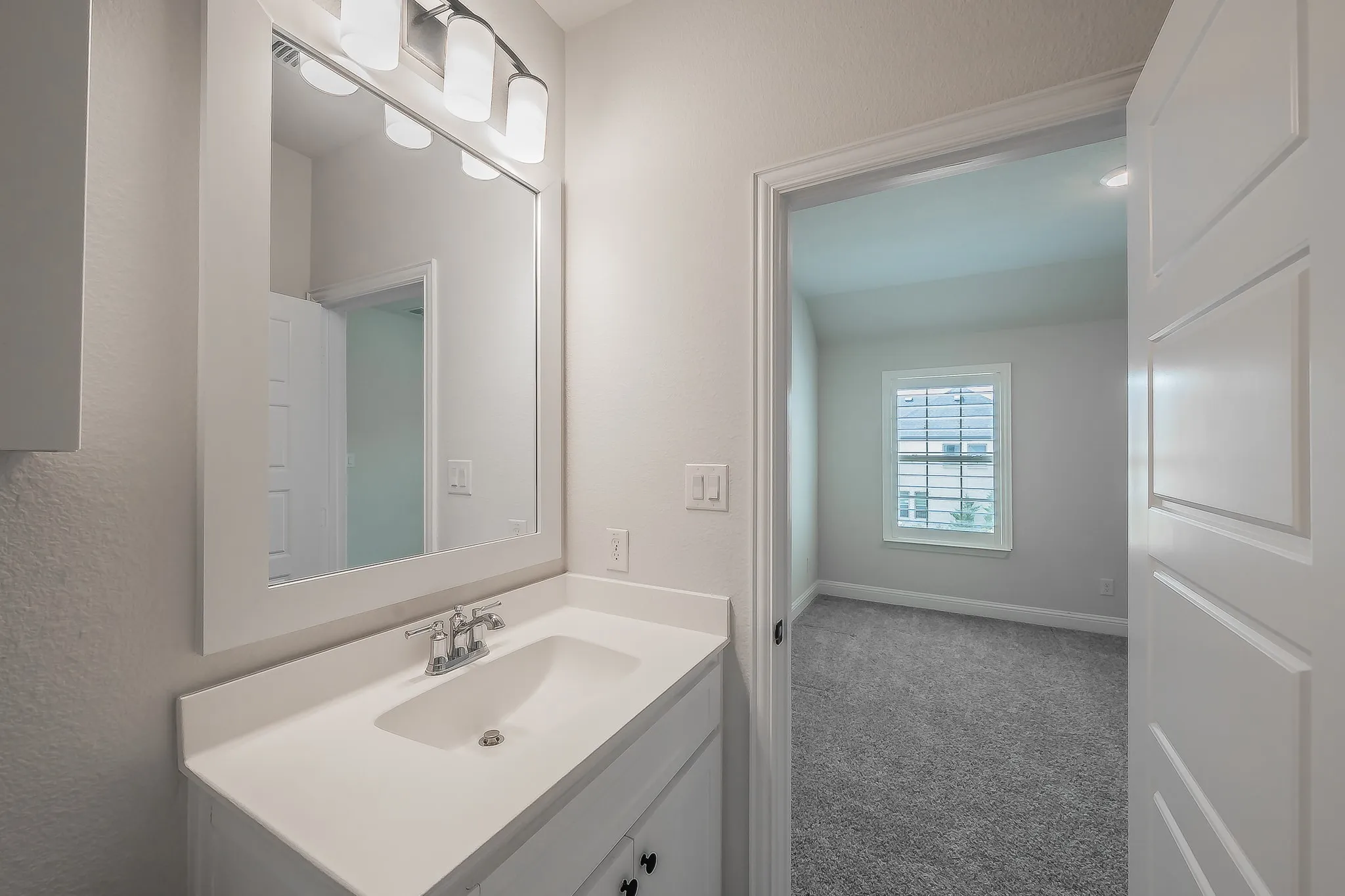 White vanity with integrated sink, chrome faucet, and a framed mirror with a four-light fixture