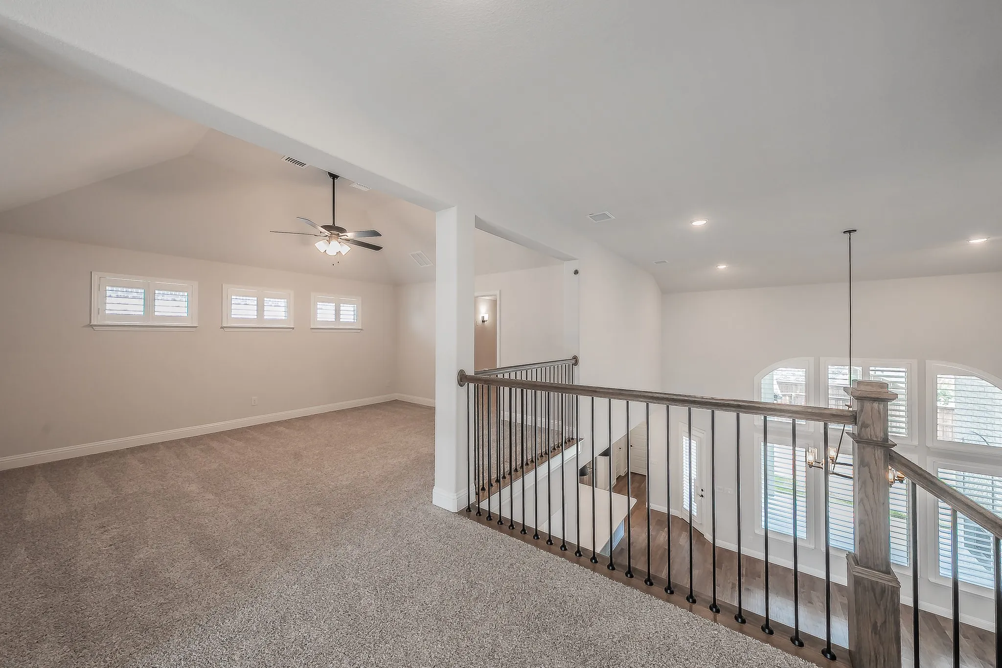 Carpeted upper-level space featuring a vaulted ceiling and a ceiling fan with integrated lighting