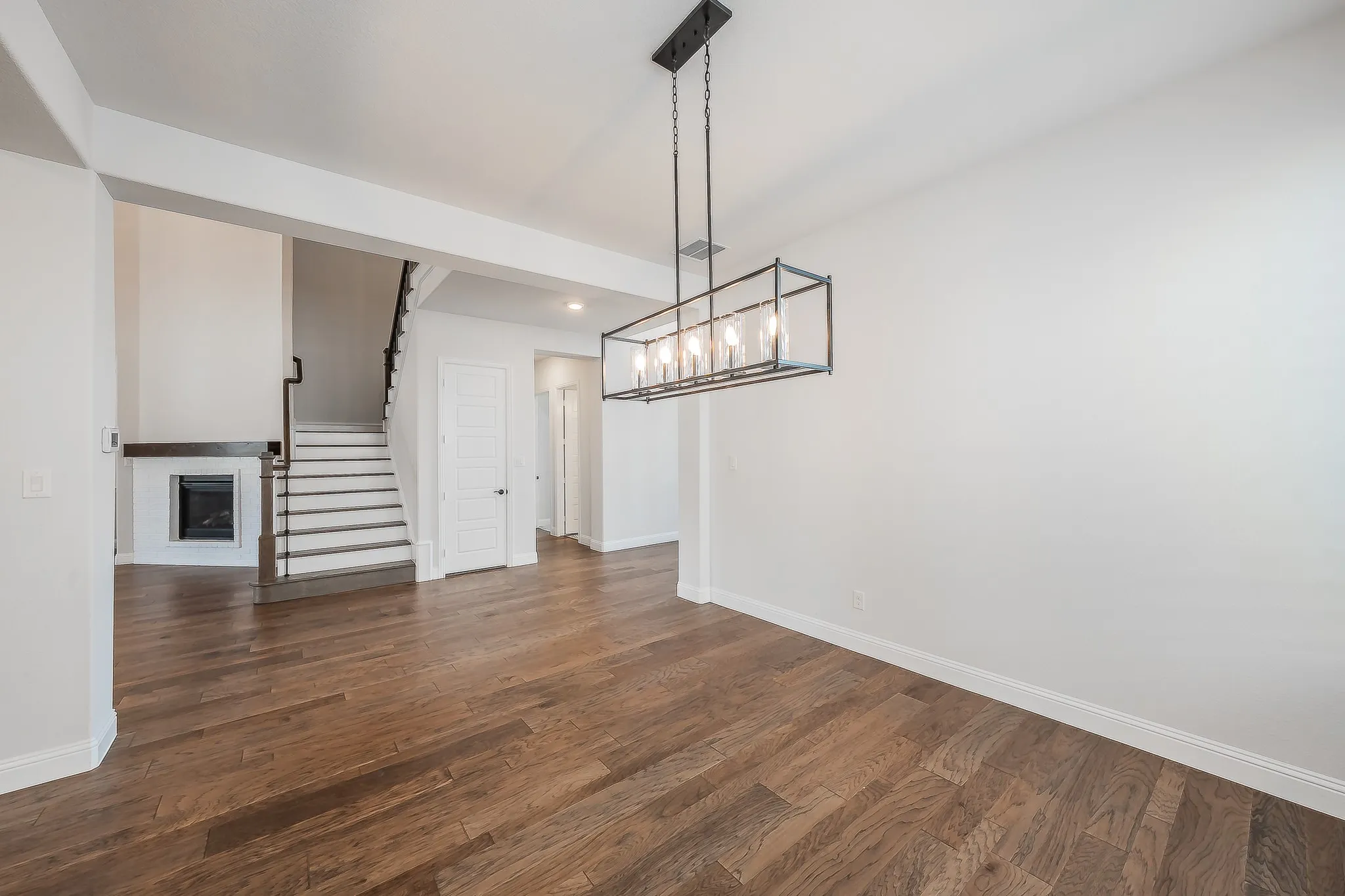 Wood-finish flooring throughout, modern fireplace with a white tile surround, dark wood mantel, and an iron baluster staircase