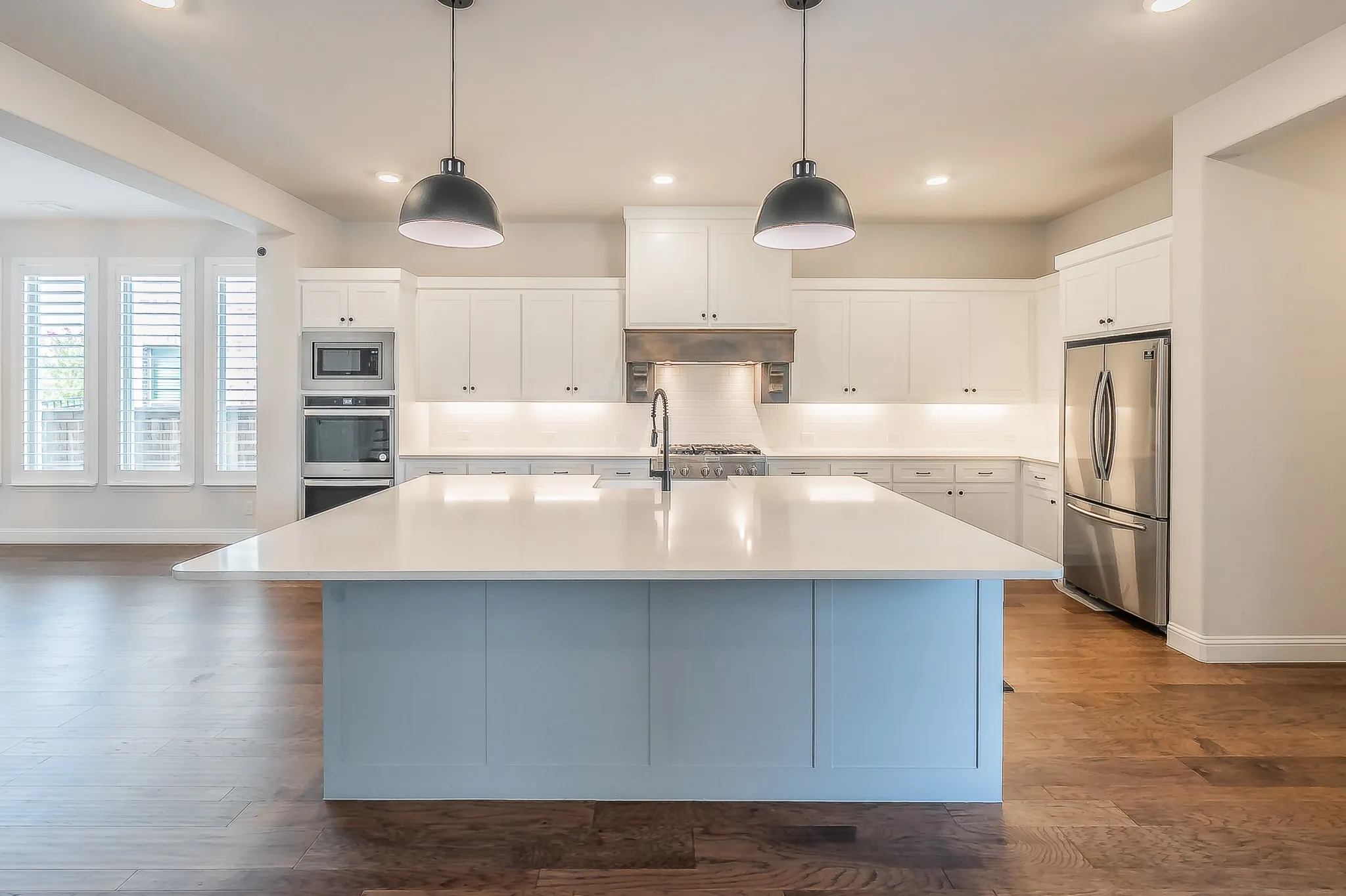 Spacious kitchen featuring an expansive central island, stainless steel appliances, abundant white cabinetry, and wood-finish flooring