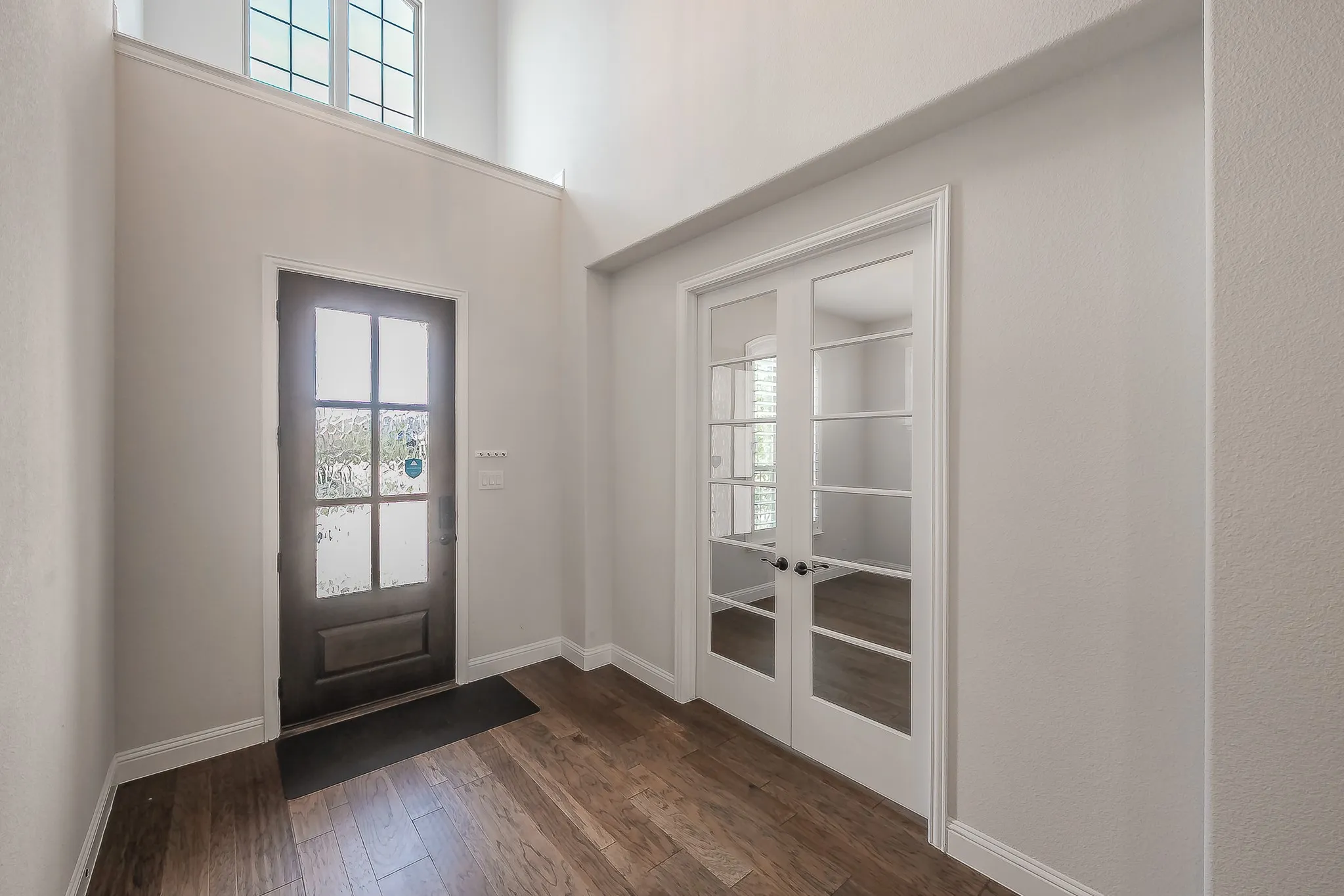 Two-story foyer with wood-finish flooring, a transom window, and white French doors leading to office.