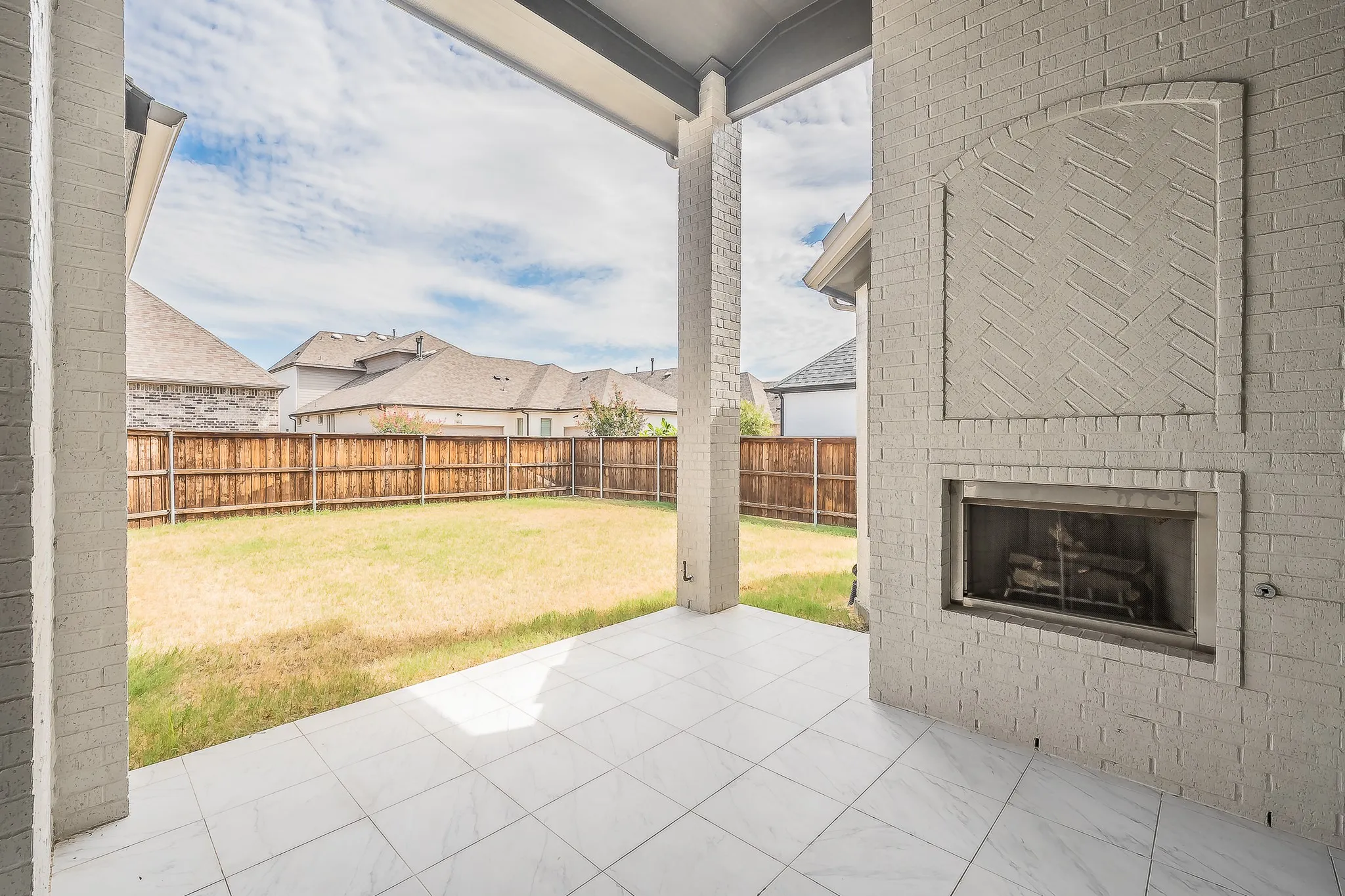 Covered patio featuring a built-in brick fireplace, tile flooring, and a fenced backyard