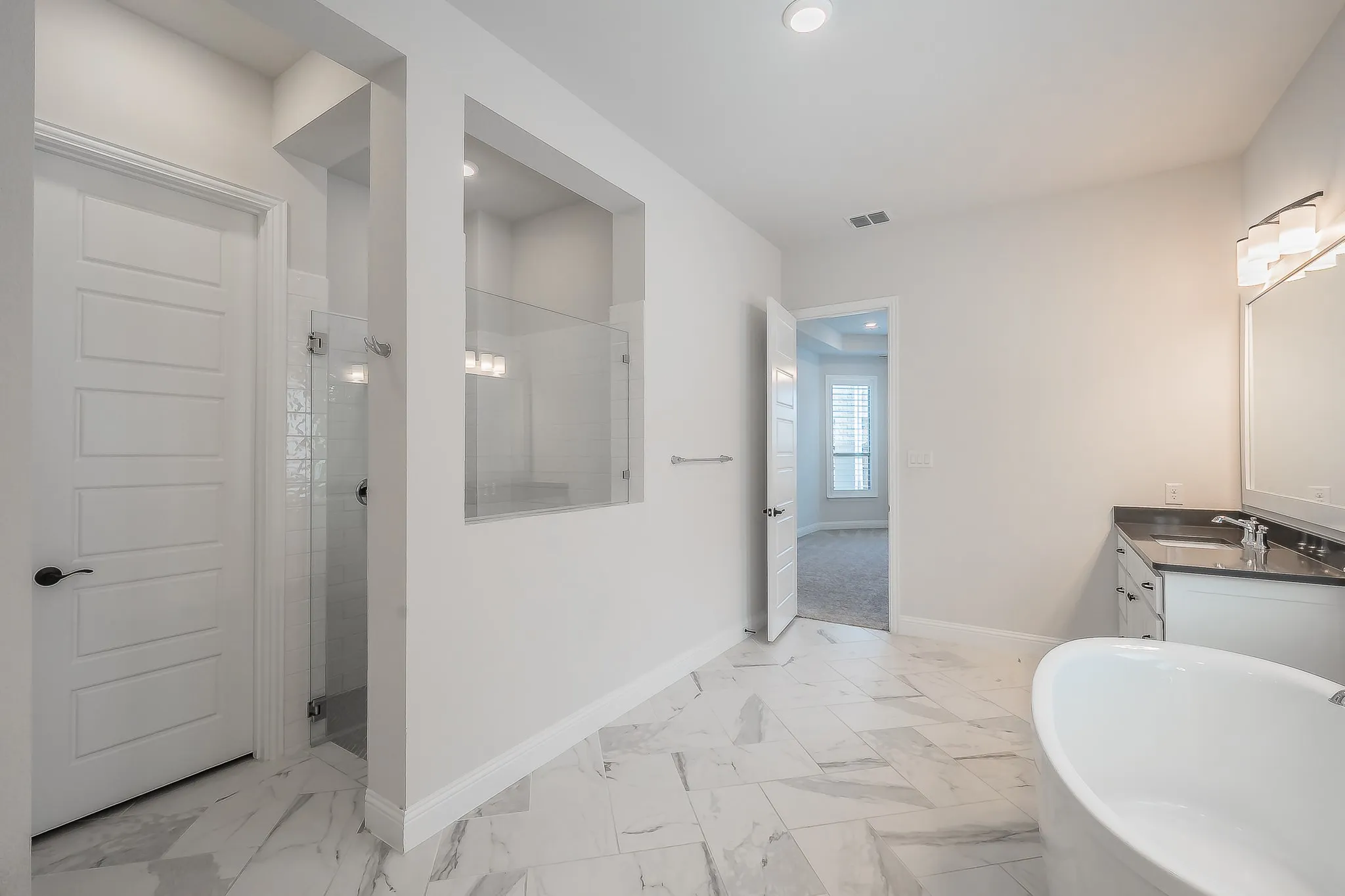 Freestanding soaking tub, walk-in shower with glass enclosure, single vanity with dark countertop, large format tile flooring, and recessed lighting