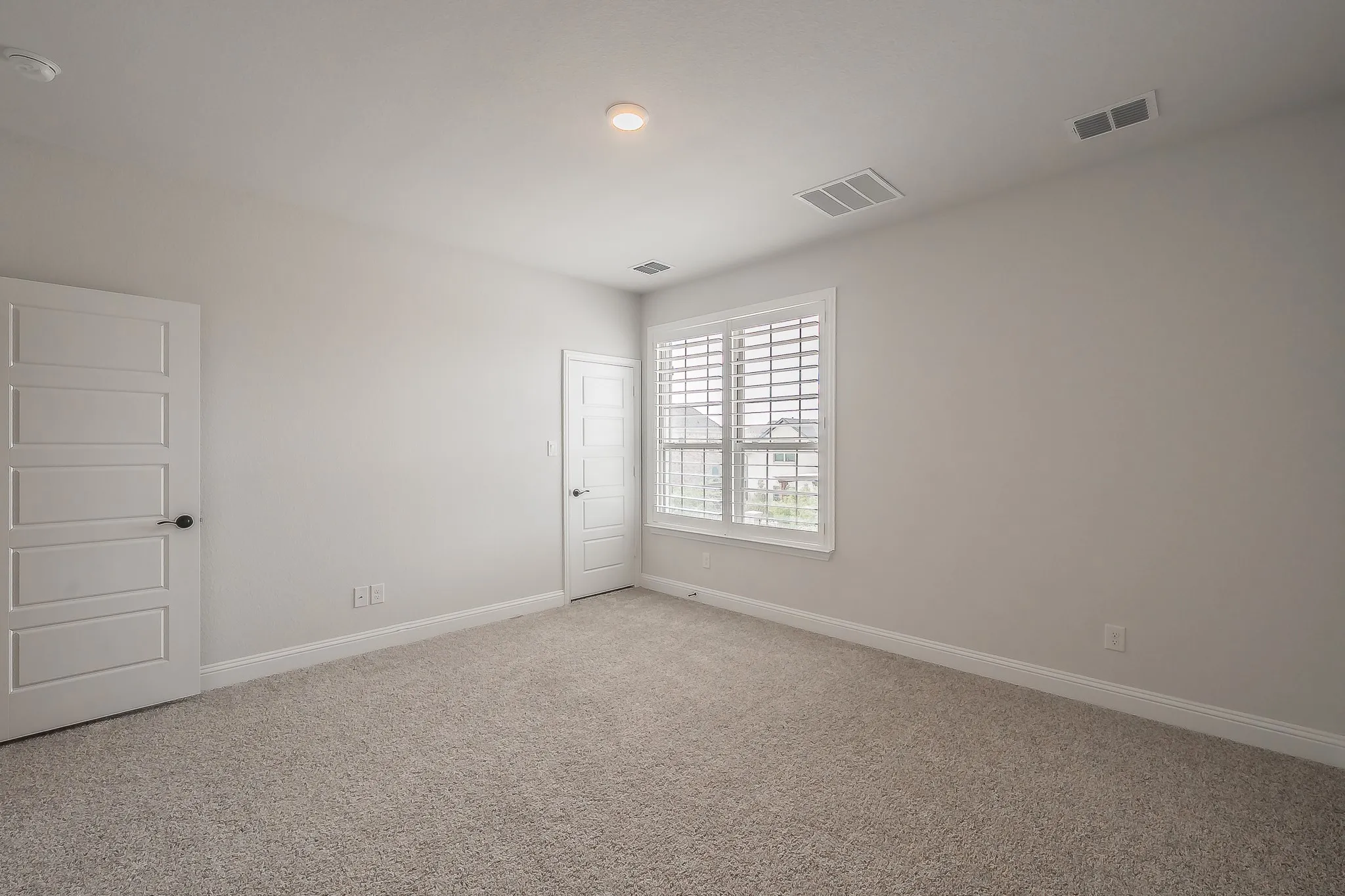 Neutral tone wall finish, plush carpet flooring, white trim details, window with white plantation shutters, and recessed ceiling lighting