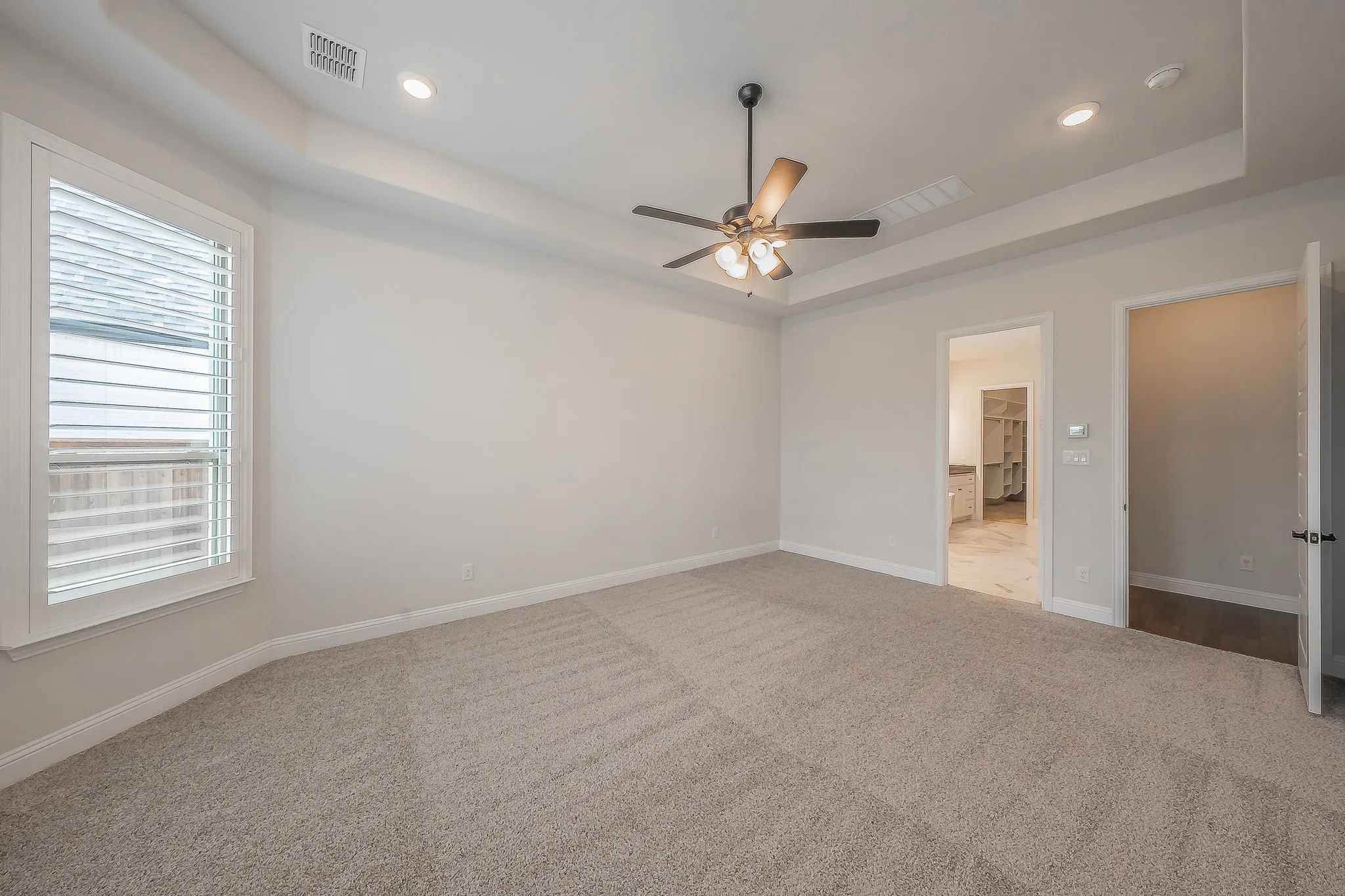 Tray ceiling, recessed lighting, ceiling fan, carpet flooring, and window with plantation shutters