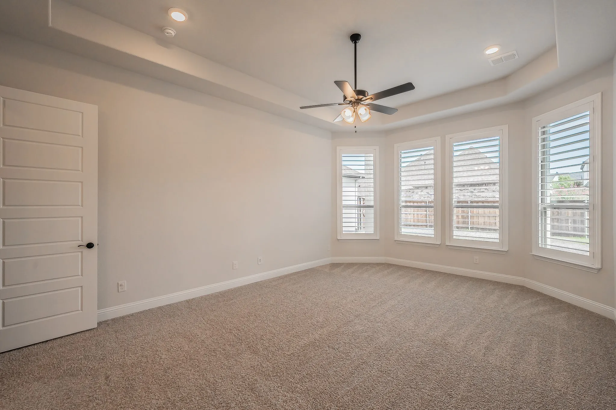 Recessed lighting, ceiling fan, carpeting, multiple windows with plantation shutters, and a tray ceiling