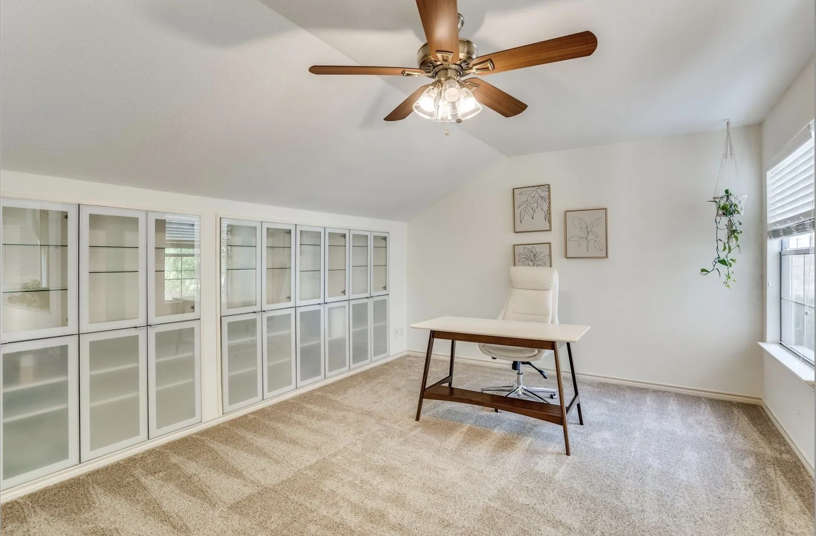 Vaulted ceiling with a ceiling fan, plush carpet, extensive built-in cabinetry with glass doors, and a window with blinds