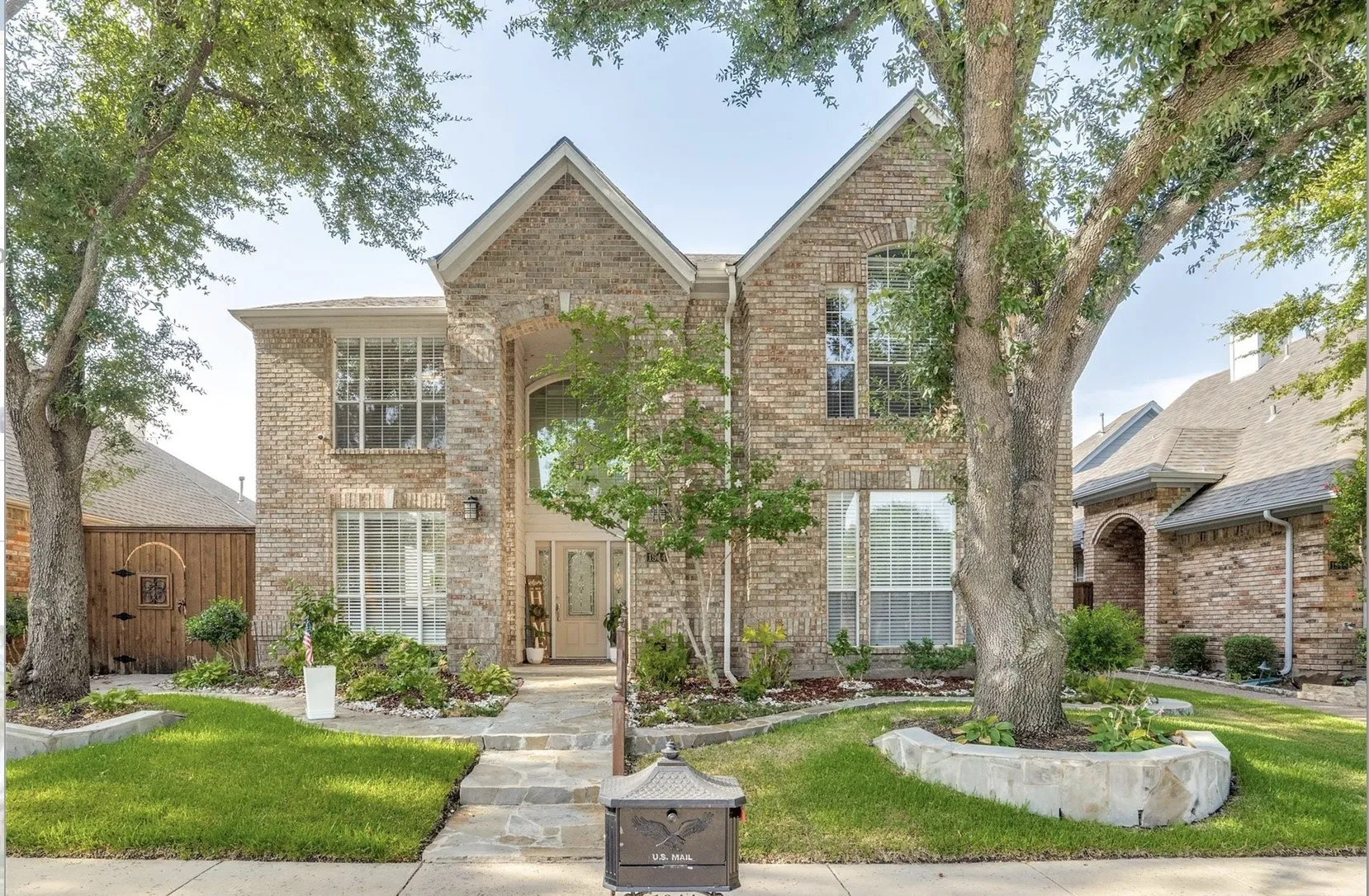 Brick facade with stone accents, mature trees, arched entryway, and a stone walkway