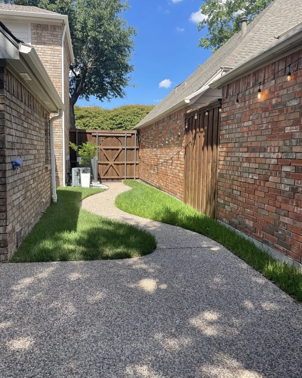 Expansive exposed aggregate walkway with a curved design, bordered by lush green landscaping