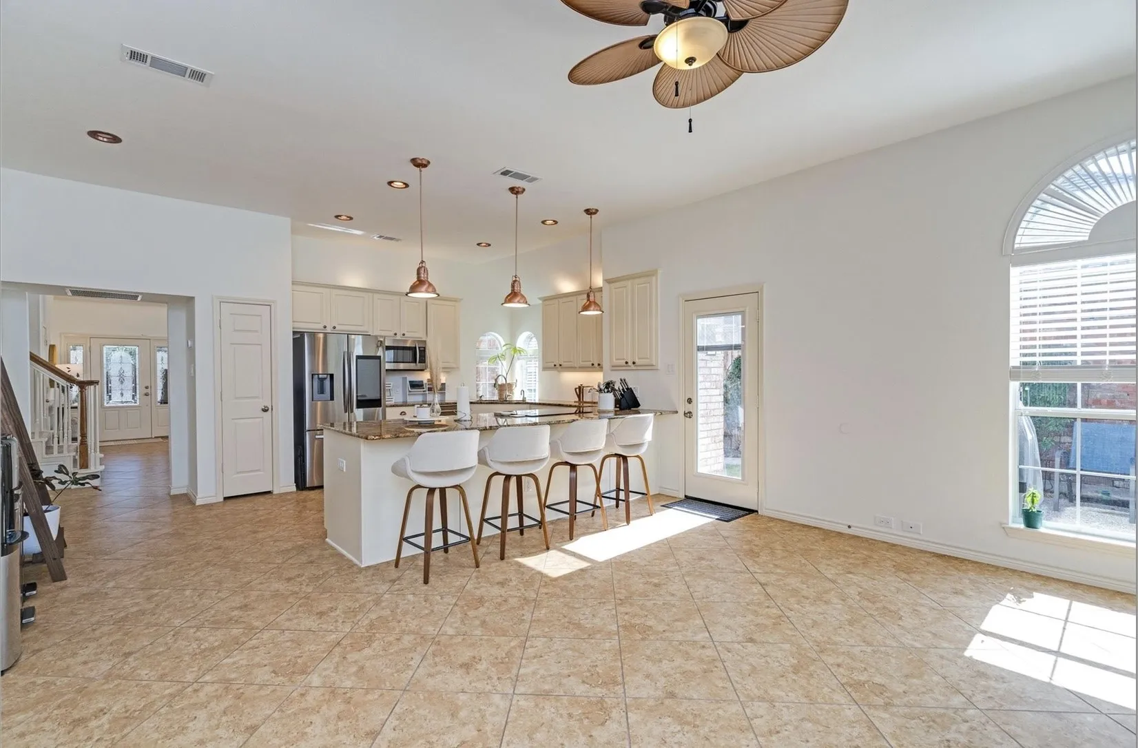 Tile flooring extending throughout, kitchen island with seating, stainless steel appliances, upper and lower cabinetry, and an arched window