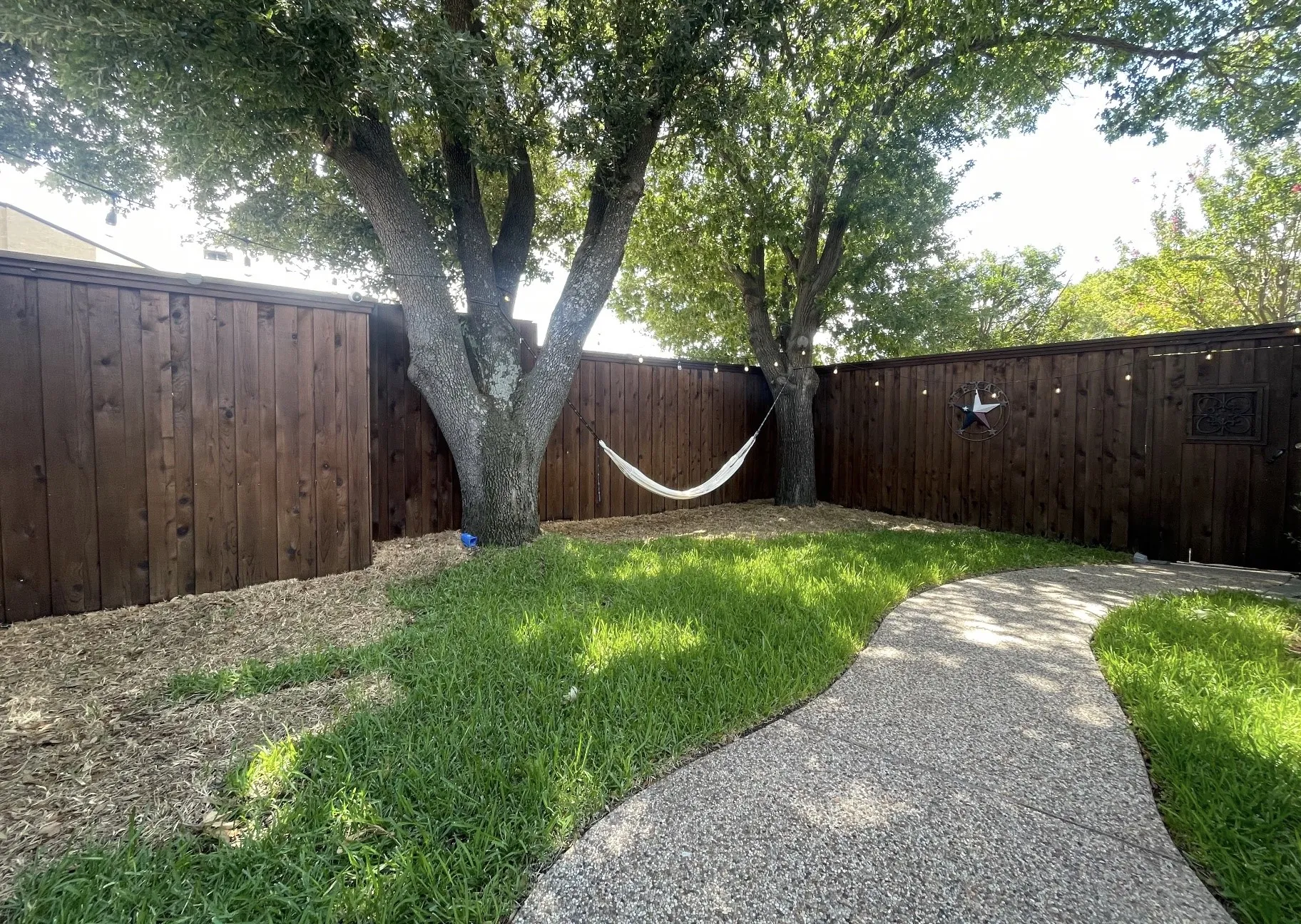 Private backyard with a stained wood fence, mature trees, and a curved concrete pathway