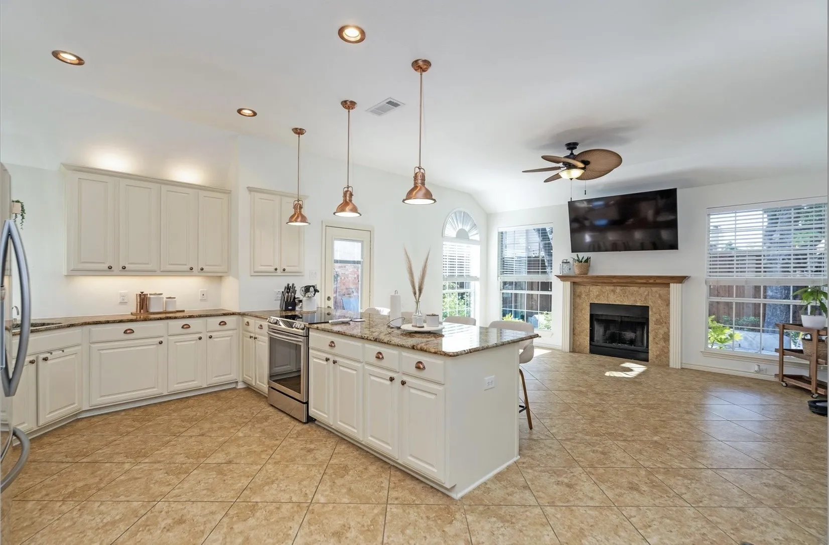 Open-concept living space with a kitchen island, recessed lighting, tile flooring, and a fireplace with a stone surround
