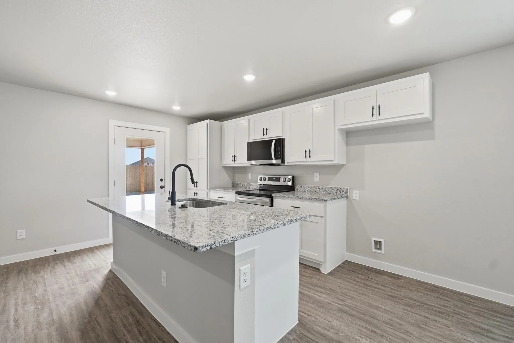 Kitchen featuring a central island with a sink, white cabinetry with black hardware, recessed lighting, wood-finish flooring, and a glass-paneled exterior door