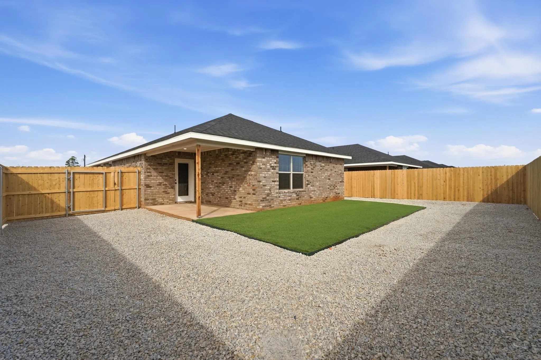 Private backyard featuring a covered patio, extensive gravel hardscaping, and a dedicated artificial turf area