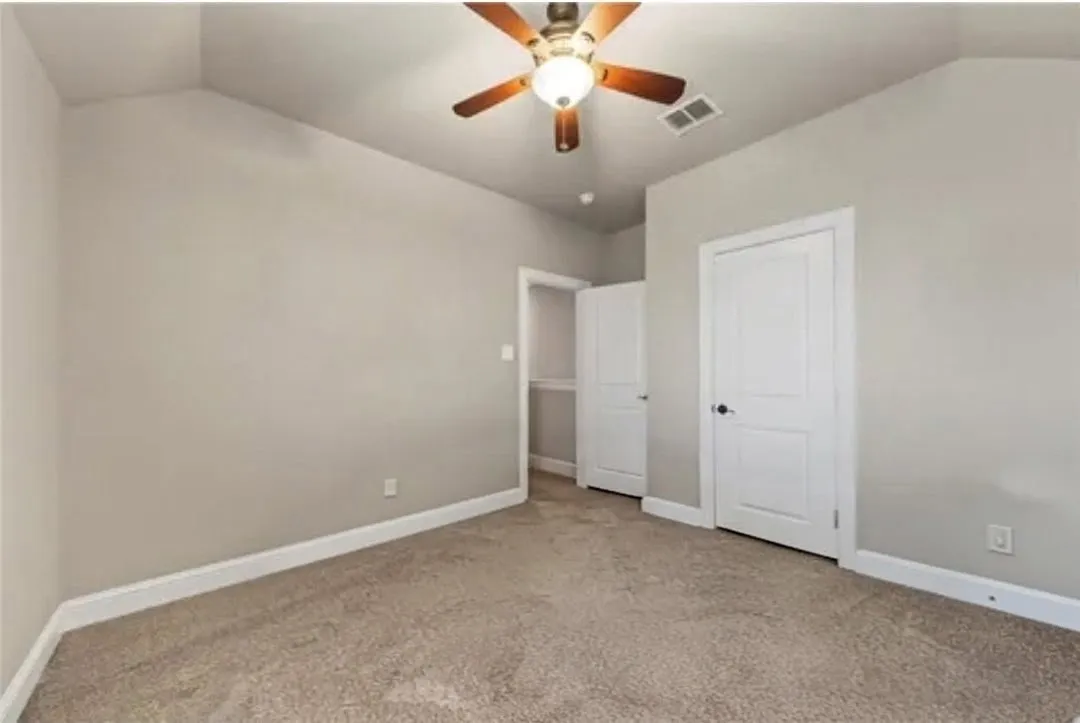 Vaulted ceiling with a ceiling fan light fixture, neutral-toned carpet, and white trim