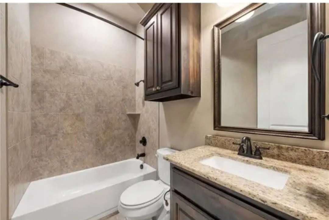 Bathroom featuring a built-in tub with tile surround, a built-in vanity with a granite-style countertop, a rectangular undermount sink, and a framed wall mirror