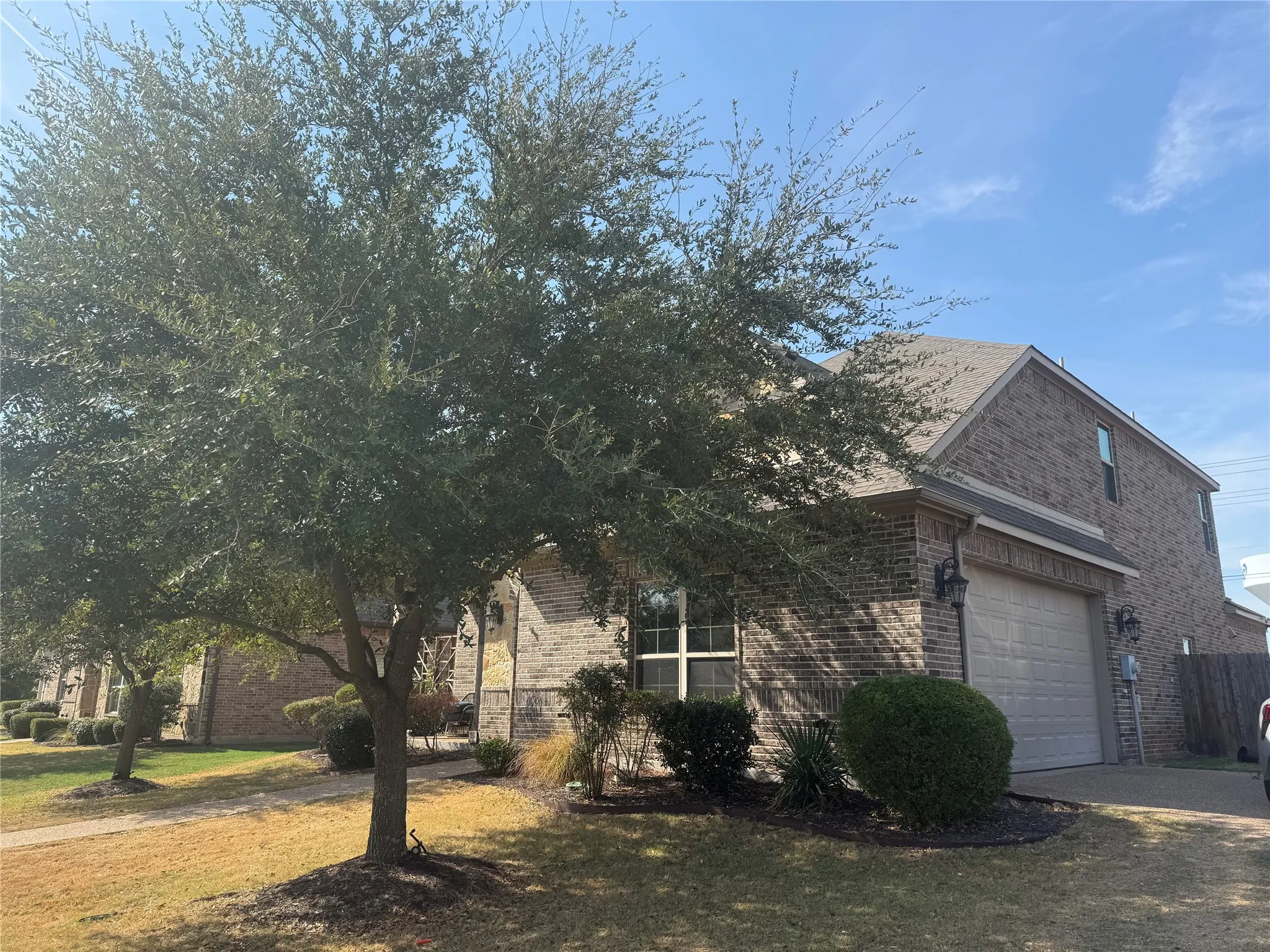Brick exterior facade with a two-car garage, mature landscaping, and a well-maintained roof