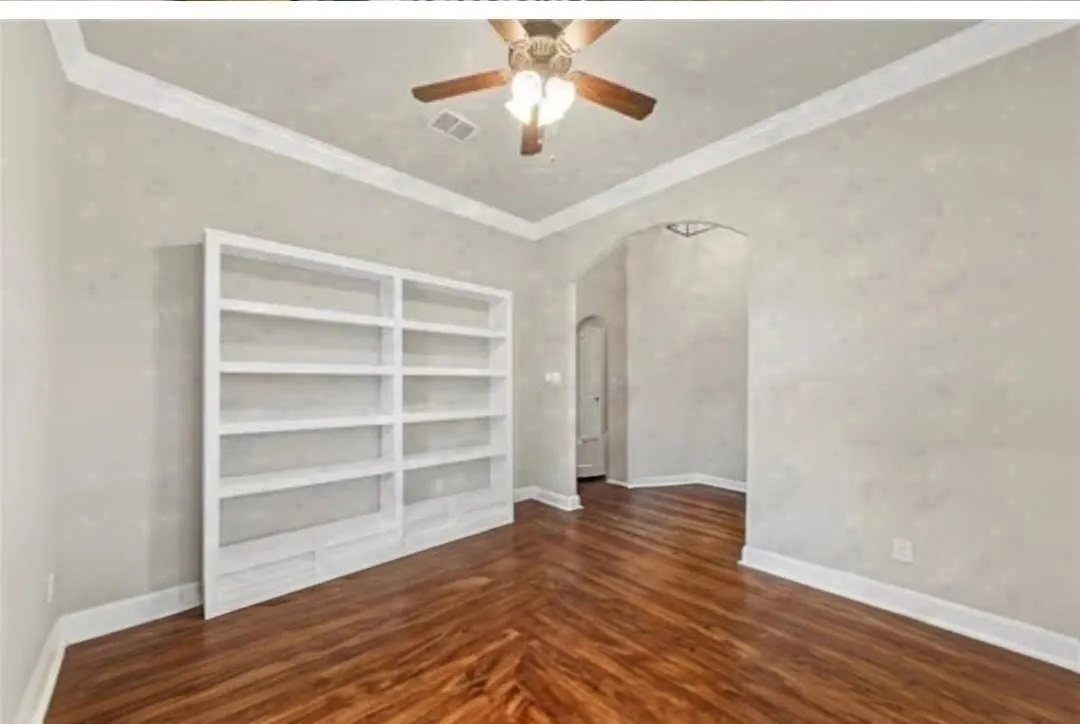 Built-in shelving, crown molding, ceiling fan, wood-finish flooring, and arched entryway