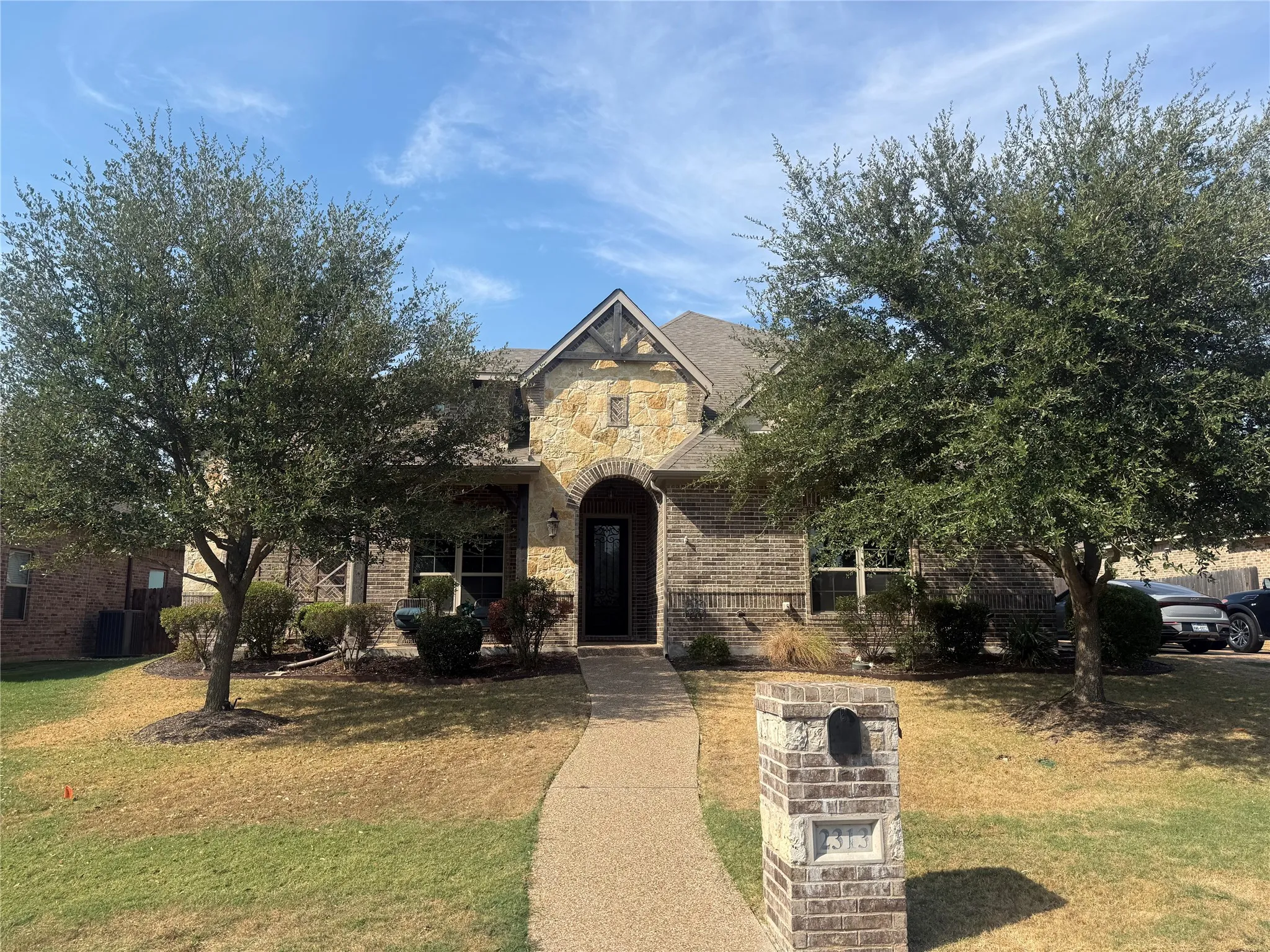 Exterior featuring a stone and brick facade, arched entryway, gabled roofline, and mature trees framing the property