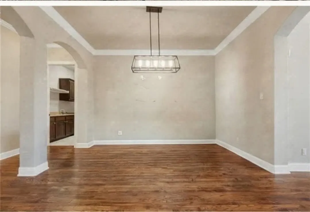 Hardwood flooring throughout, featuring crown molding, a modern linear chandelier, and arched doorways