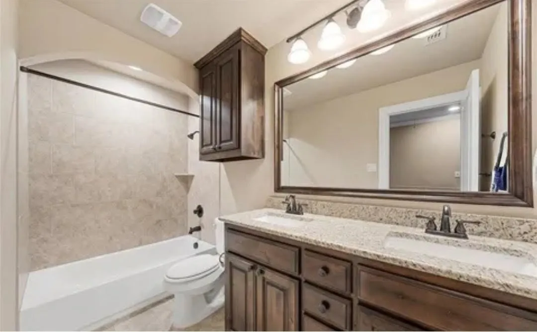 Dual vanity with granite countertops, rich wood cabinetry, and a framed mirror