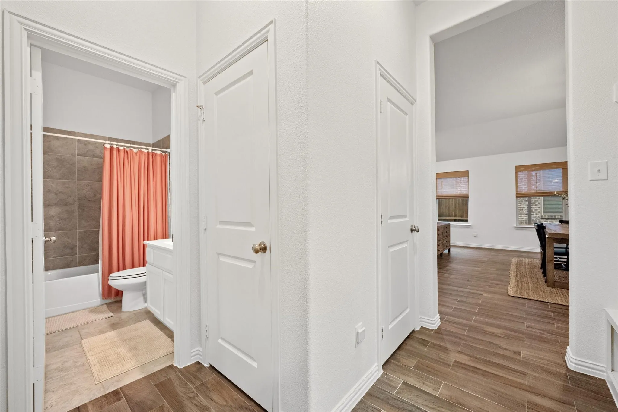 Wood-finish flooring throughout, white interior doors, and a bathroom featuring a white vanity with integrated sink, a white toilet, and tub with tiled surround