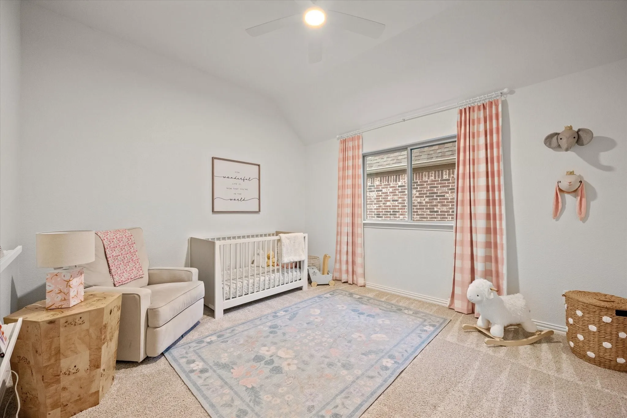 Vaulted ceiling, ceiling fan with integrated lighting, light-toned carpeting, window with brick-patterned exterior, and white interior walls